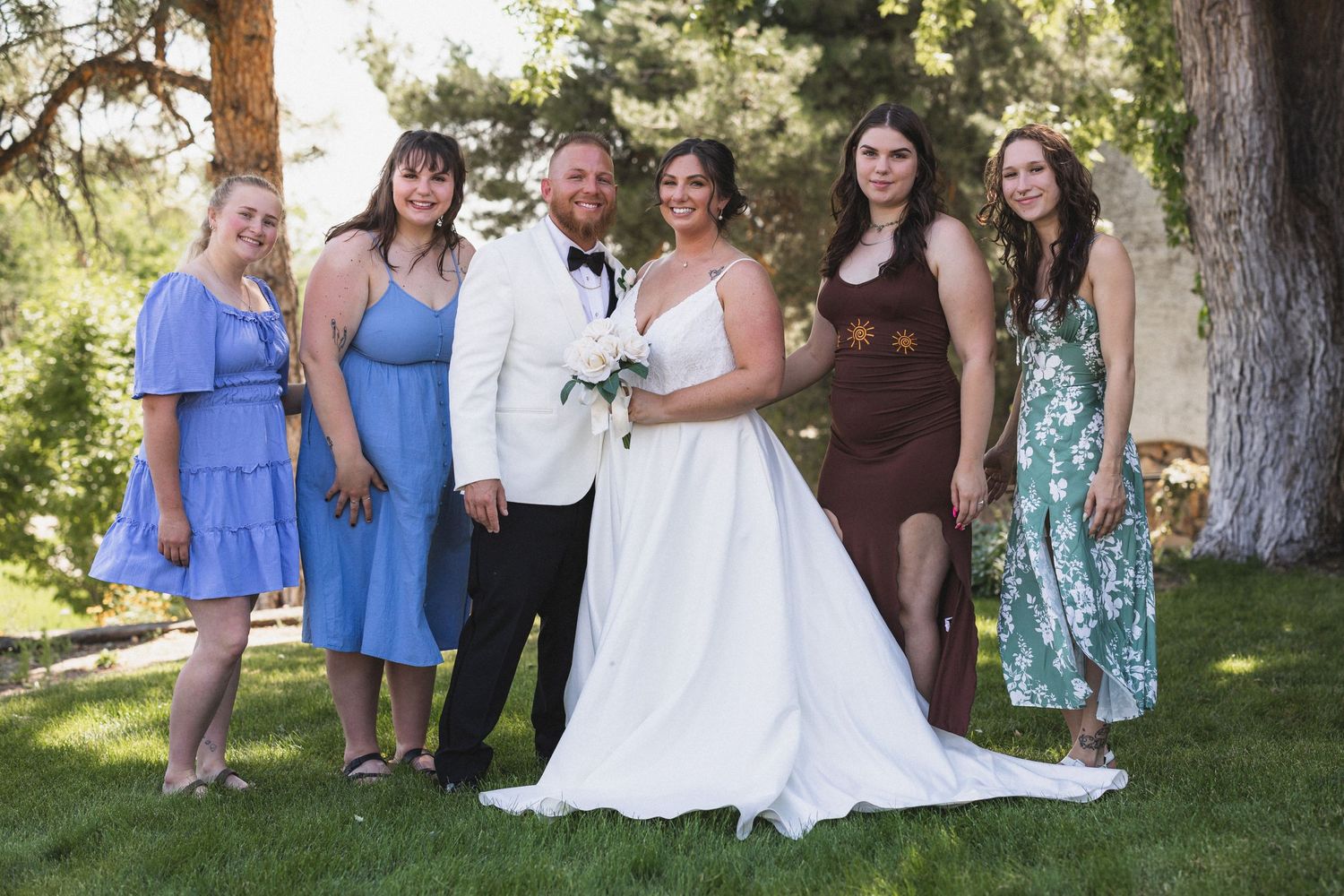 Wedding group photo with bridesmaids in blue and brown dresses gathered outdoors.