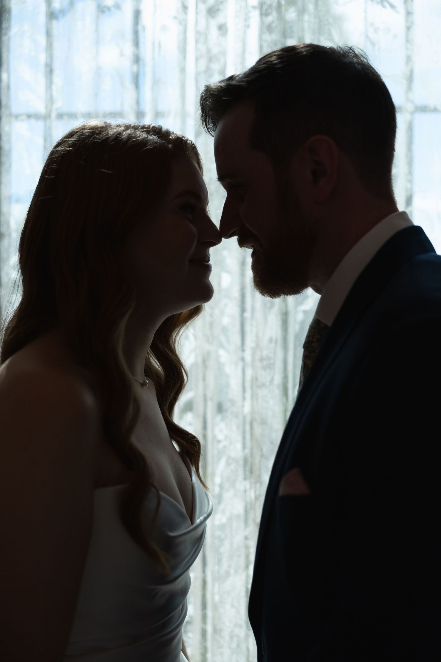 Romantic silhouettes of a couple in formal attire share intimate moments against a bright window backdrop.