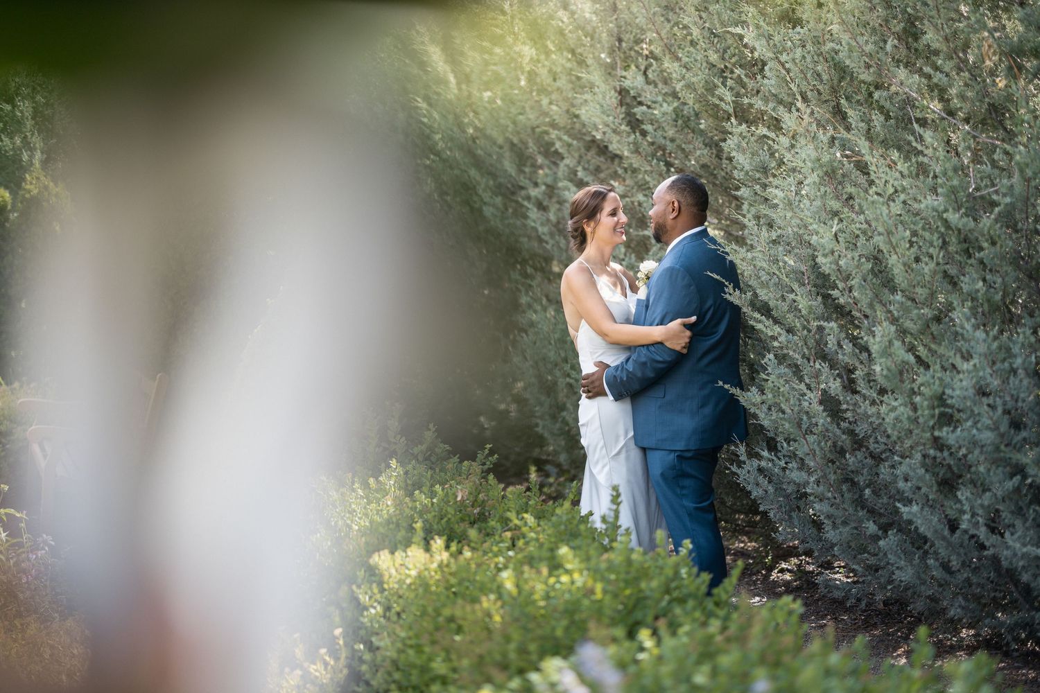 A romantic garden photoshoot with a couple in formal attire among flowering bushes.