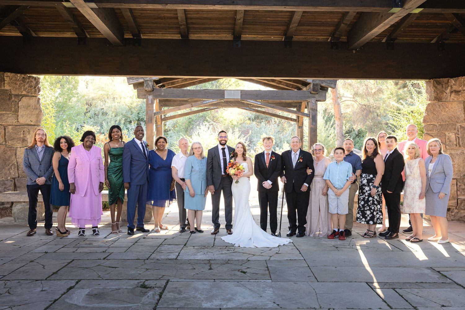 Large wedding party group photo under rustic stone archway.