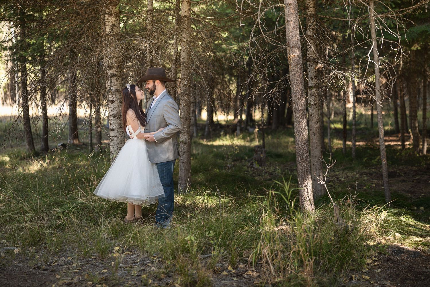 Romantic woodland wedding portrait among tall pine trees in natural lighting.