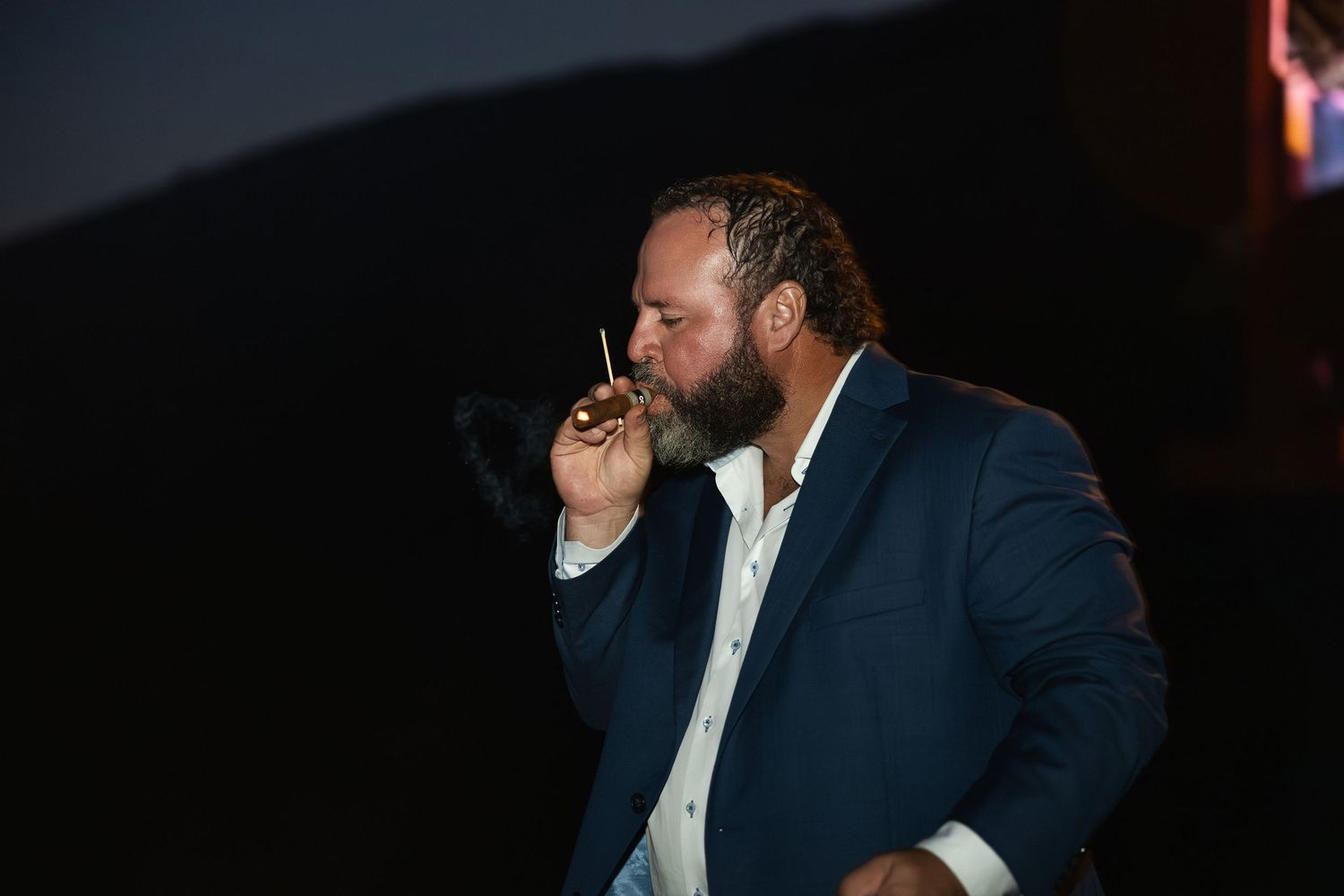 Wedding party members sharing a moment with cigars at twilight.