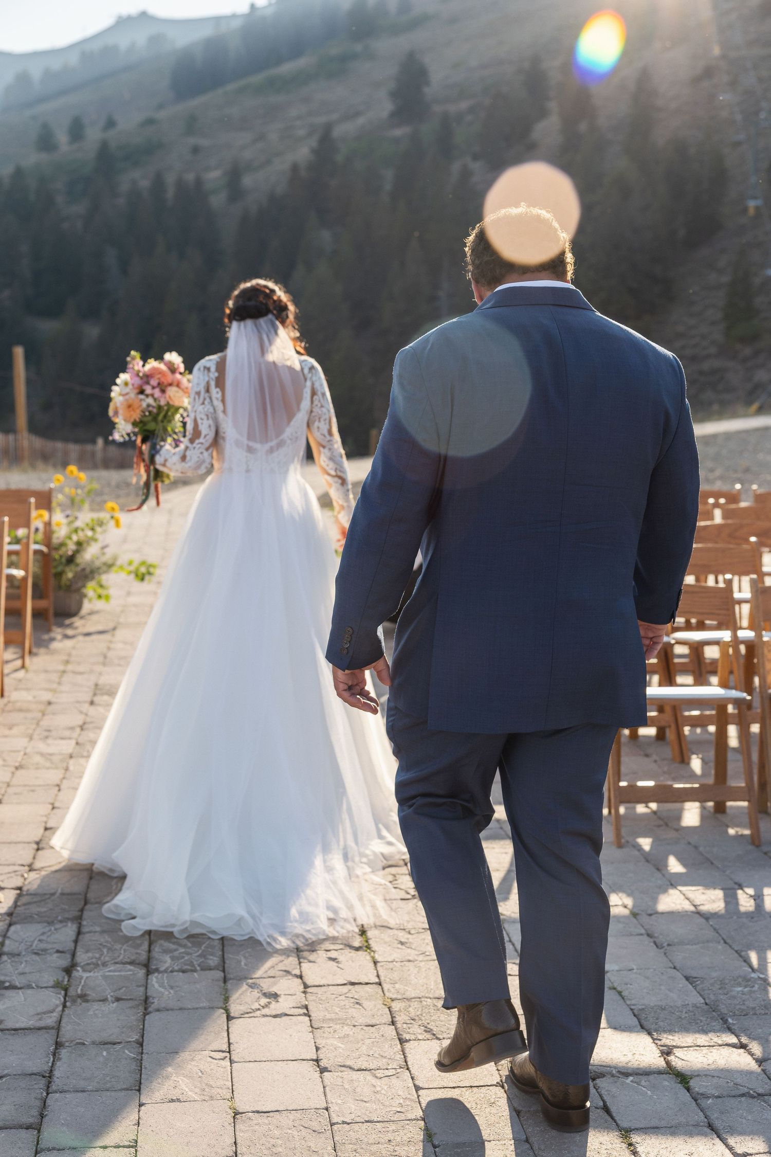 Wedding couple walking on stone patio with mountain views at sunset.