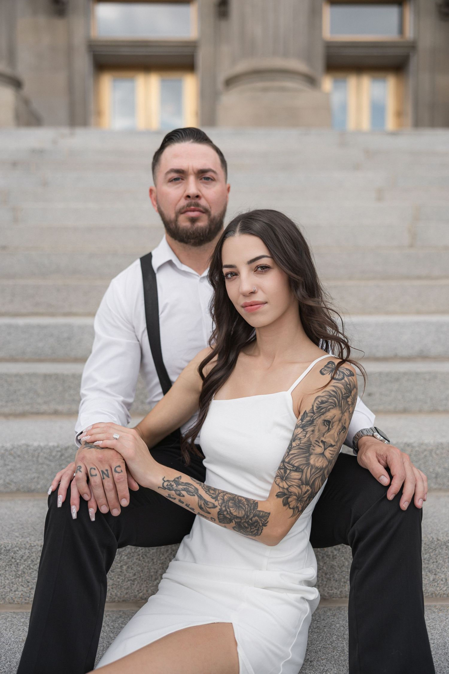 Stylish couple in contrasting black and white outfits poses on stone steps showing tattoo artwork.