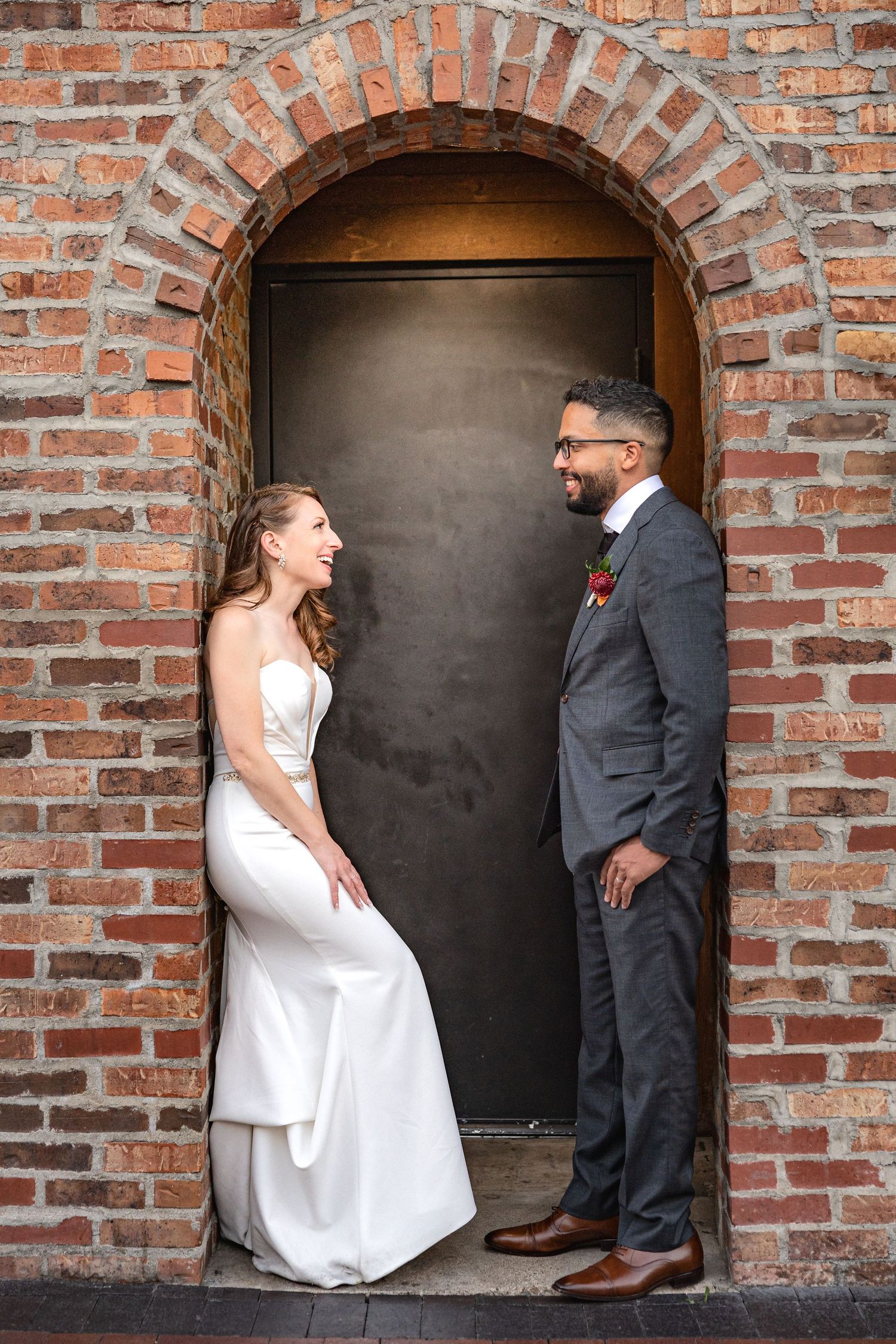 Bride and groom share a moment in a brick archway doorframe.