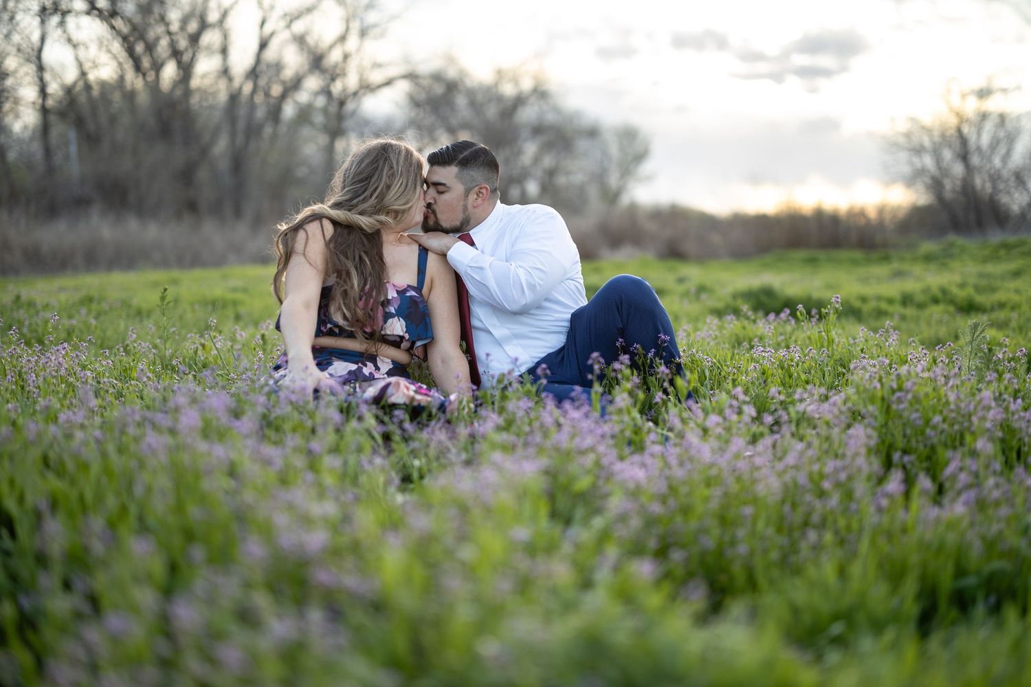 Romantic couple sits together in a blooming spring meadow during golden hour.
