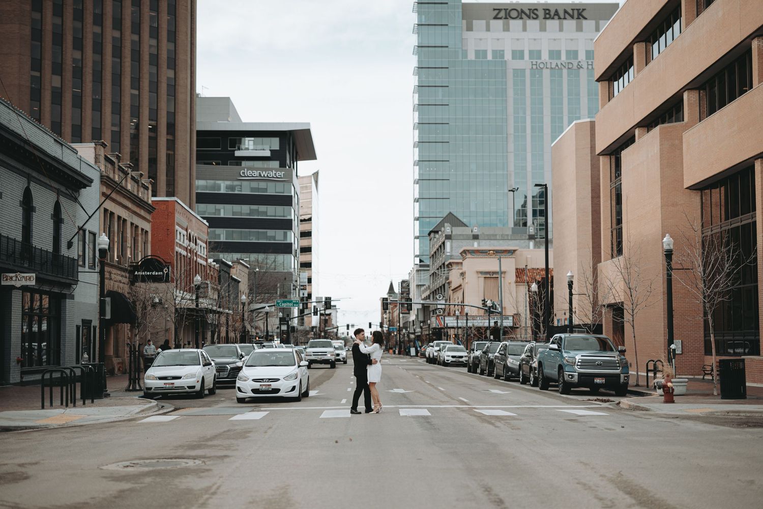 Urban street scene with tall buildings and parked cars along a city road.