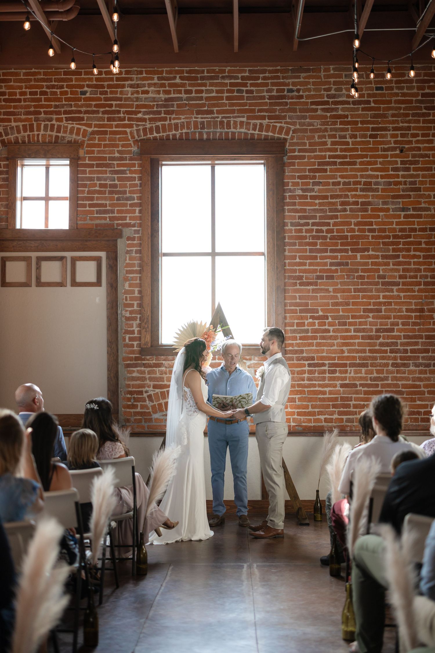 Wedding ceremony in rustic brick venue with natural light streaming through tall windows.