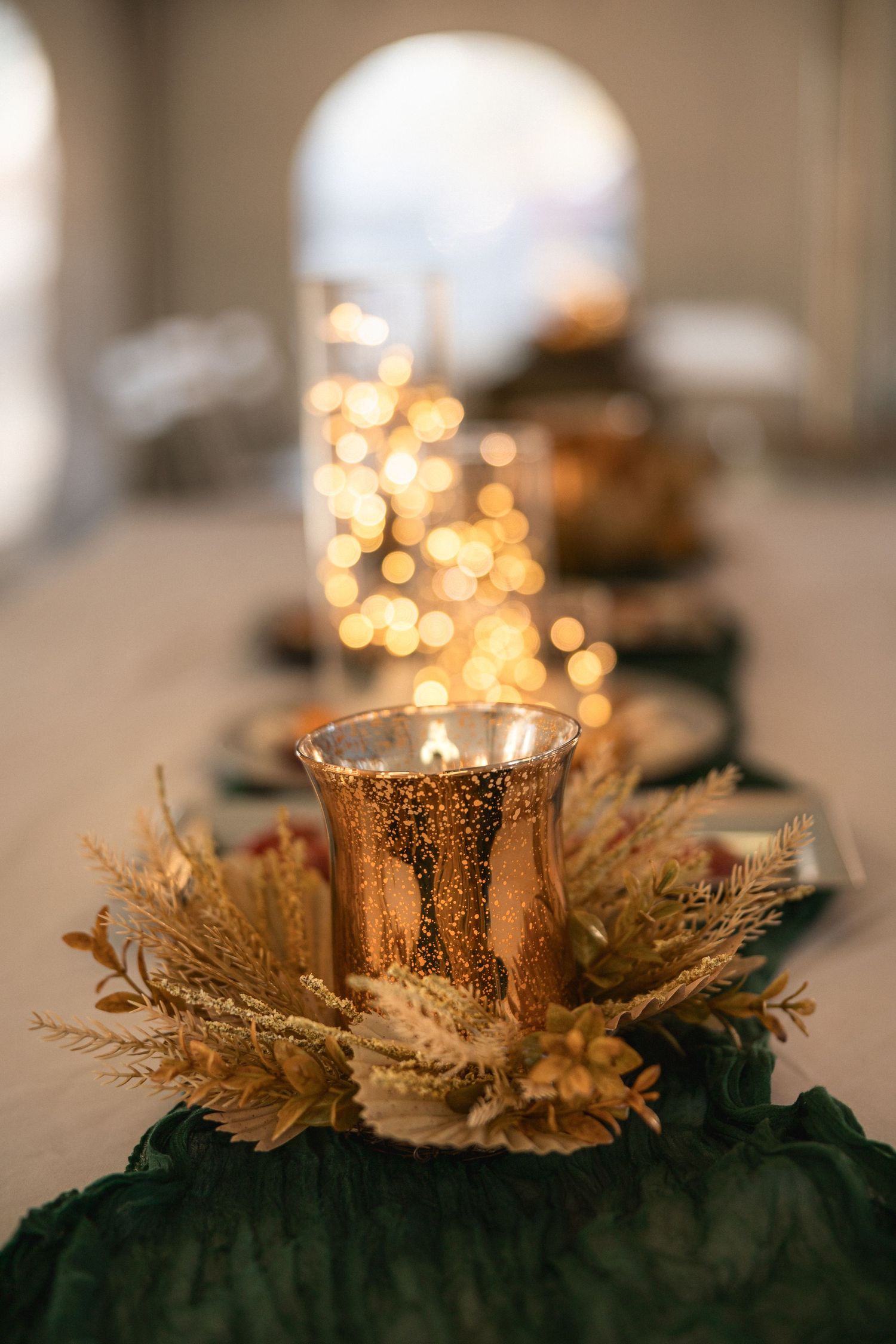Glowing gold mercury glass candle holder with dried flowers creates elegant wedding table centerpiece.