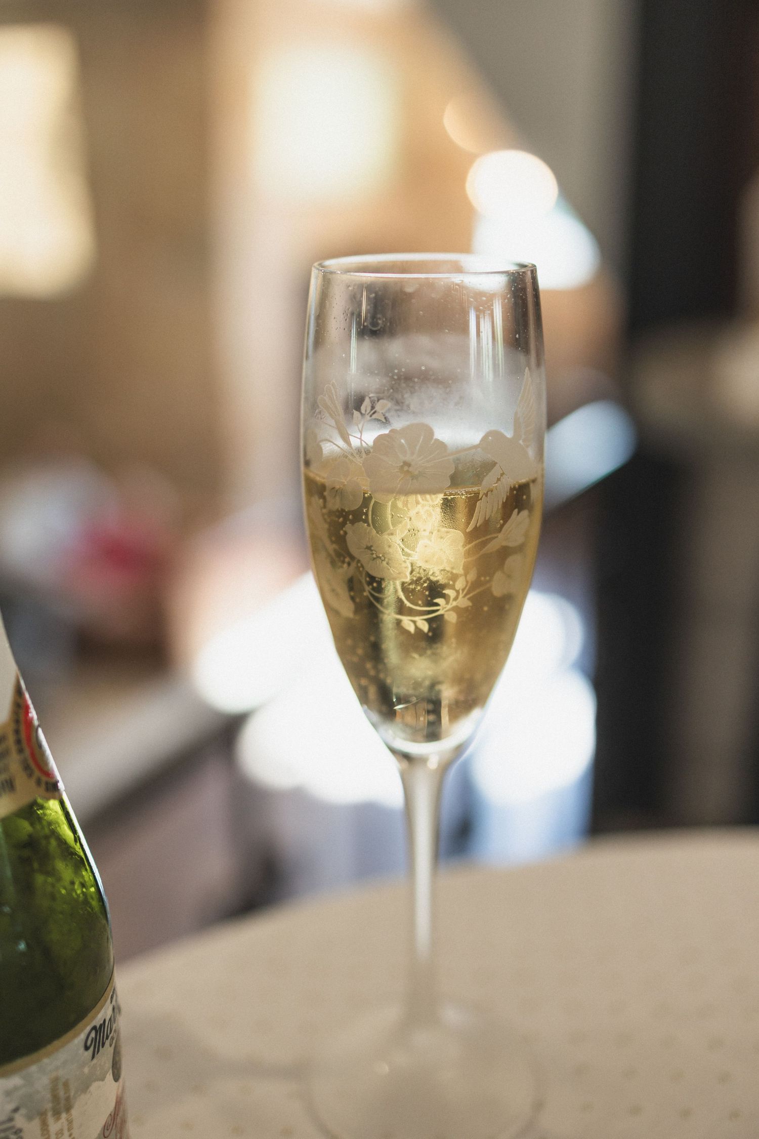 A glass of champagne sits elegantly on a table with soft bokeh lighting in the background.