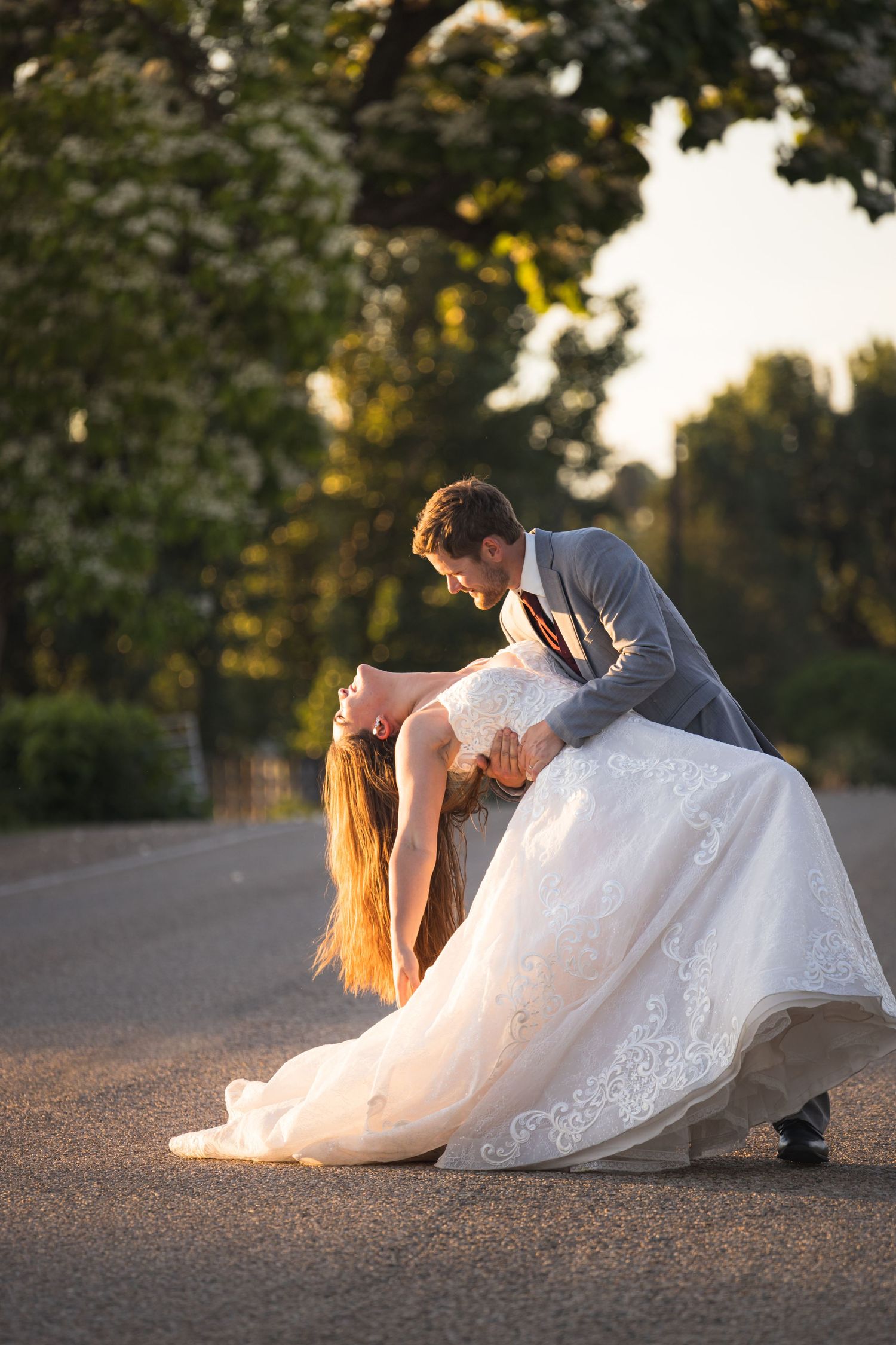 A dramatic dip pose between newlyweds on a paved path at sunset.
