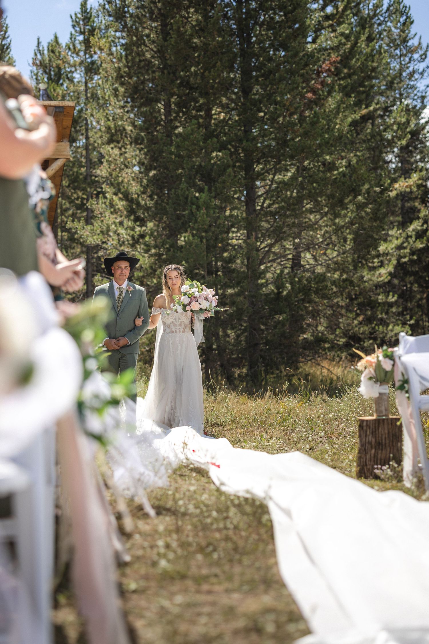 Rustic outdoor forest wedding ceremony with couple standing at altar on white aisle runner.