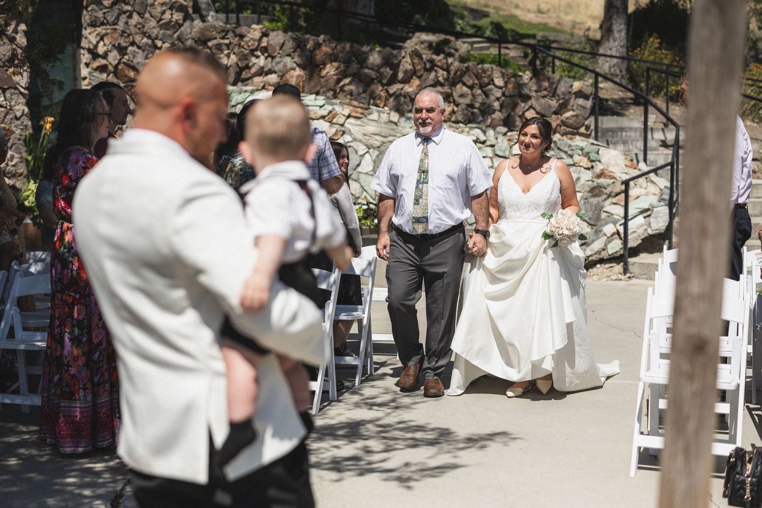 Wedding ceremony guests watch as the bride walks down the aisle at an outdoor venue.