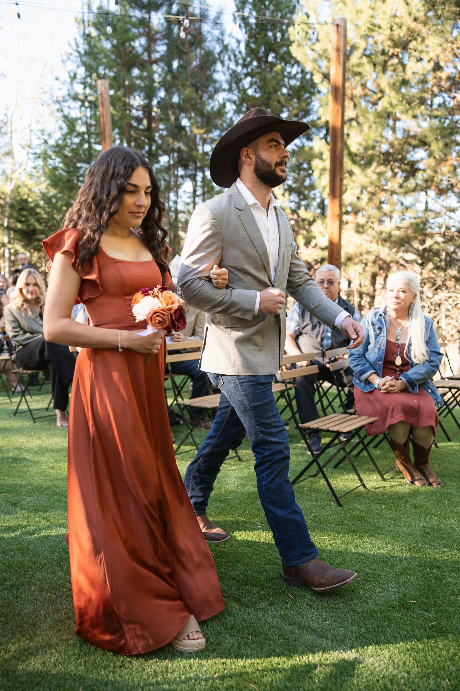 Wedding party dancing on green lawn wearing burgundy dresses and western attire.
