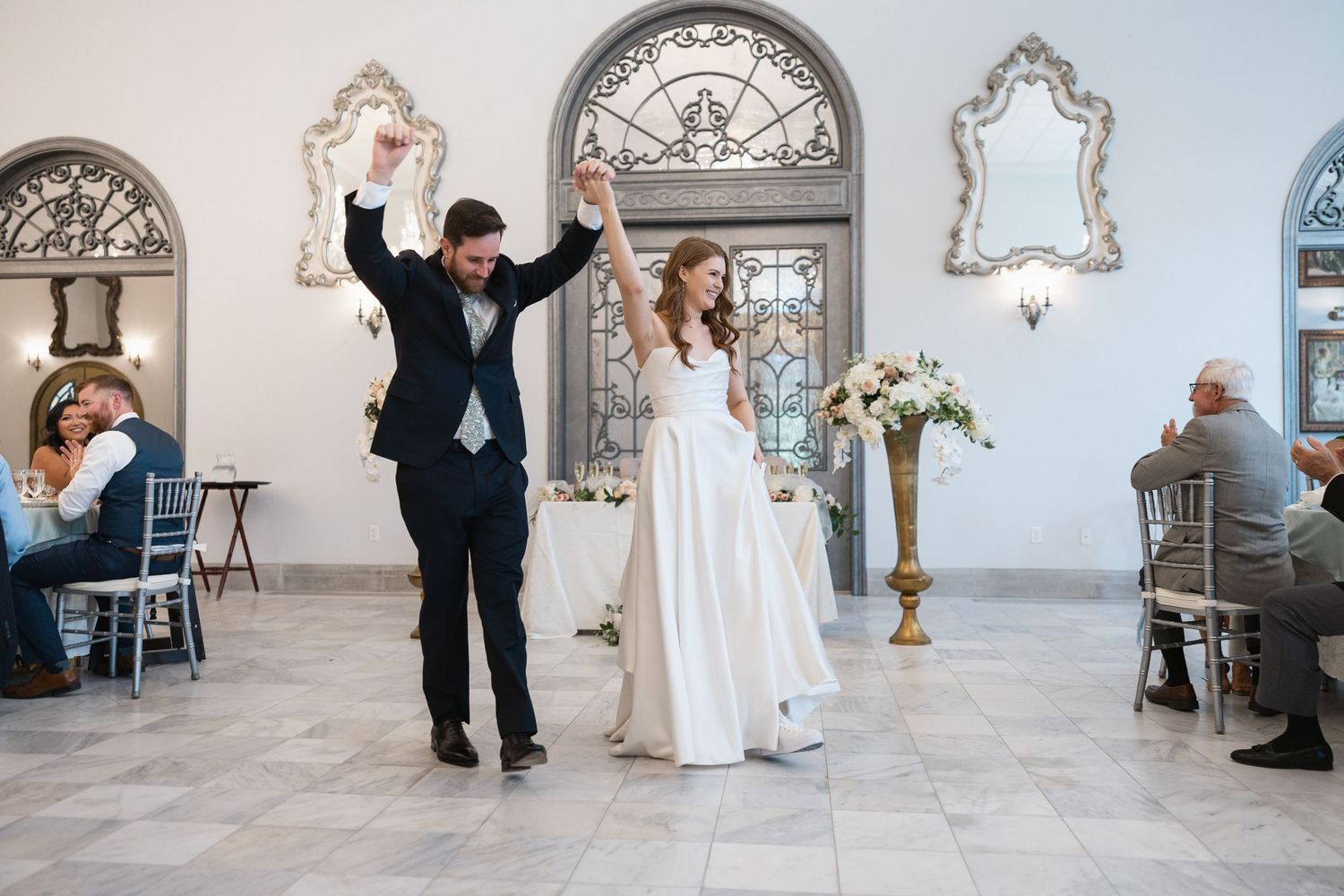 Wedding celebration moments captured in an elegant white room with ornate mirrors and floral decor.