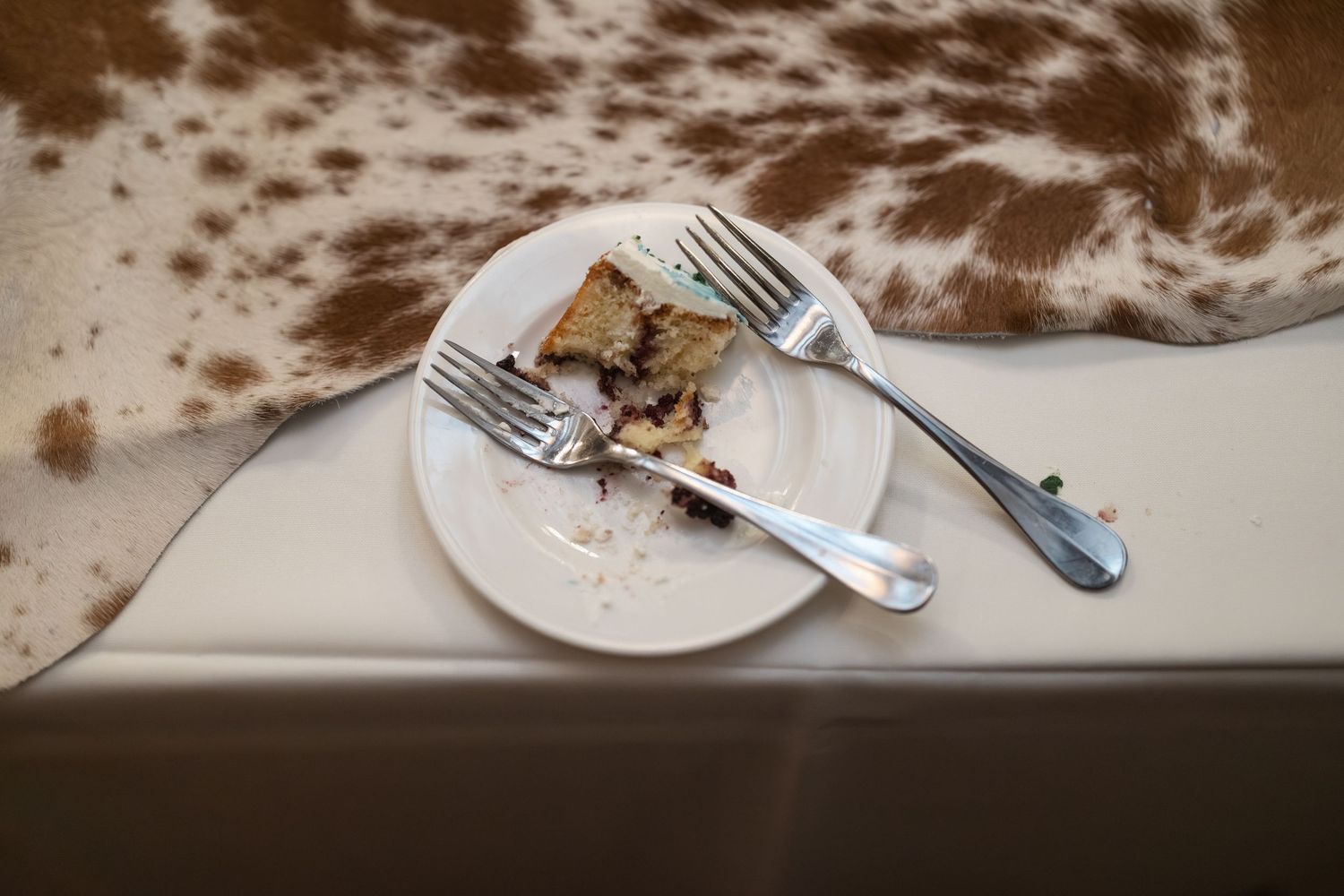 Empty plate with used silverware and cake crumbs on a white tablecloth.