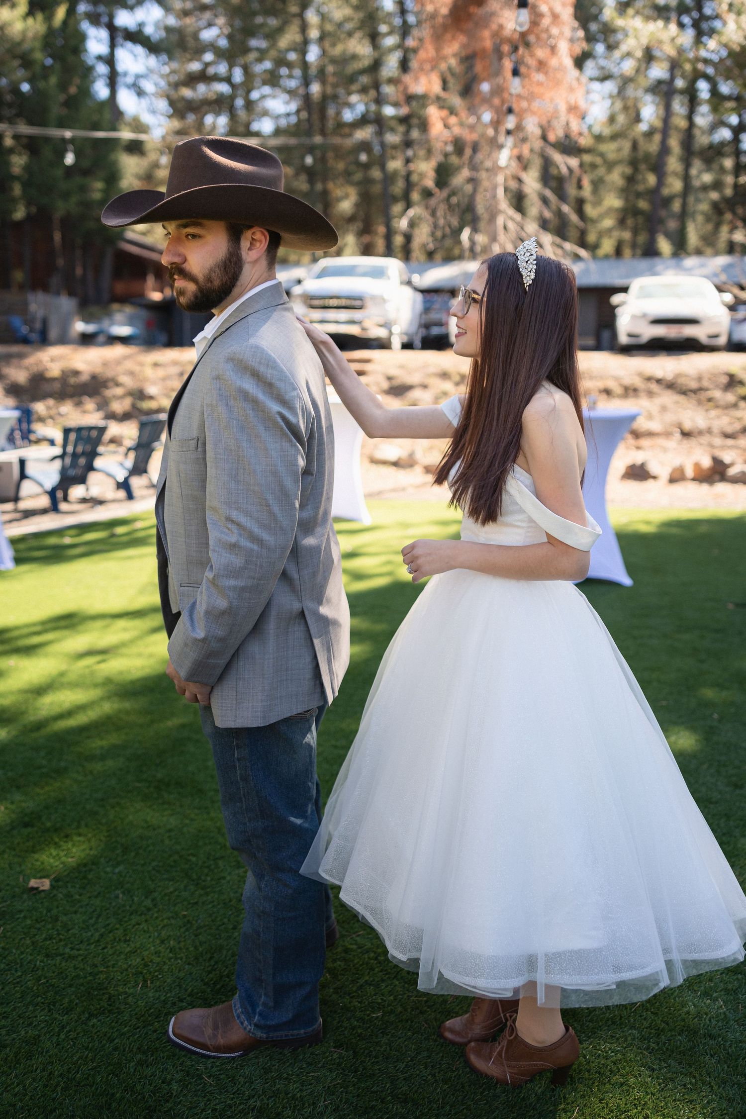 Couple in western wedding attire sharing a romantic moment on green lawn.
