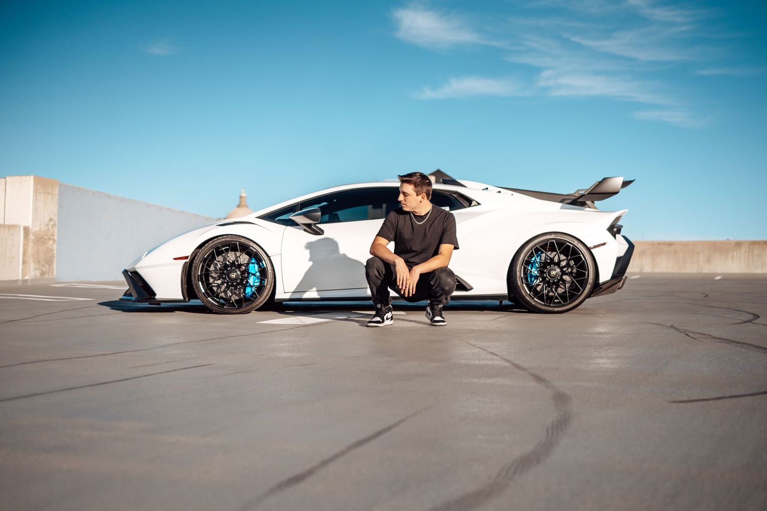Stylish pose with white Lamborghini supercar against blue sky on urban rooftop.