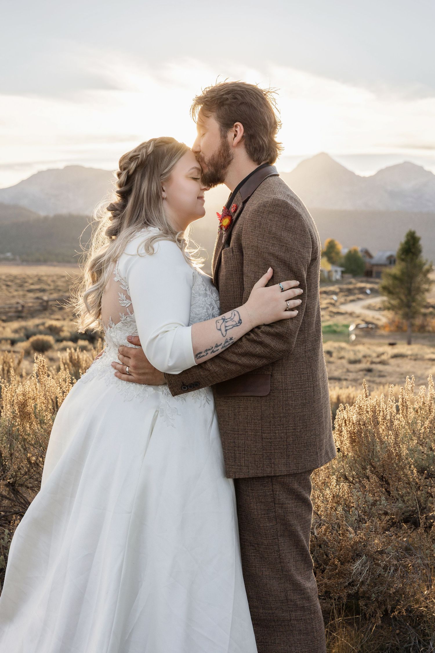 A couple embraces during their wedding photoshoot against a mountain backdrop at sunset.