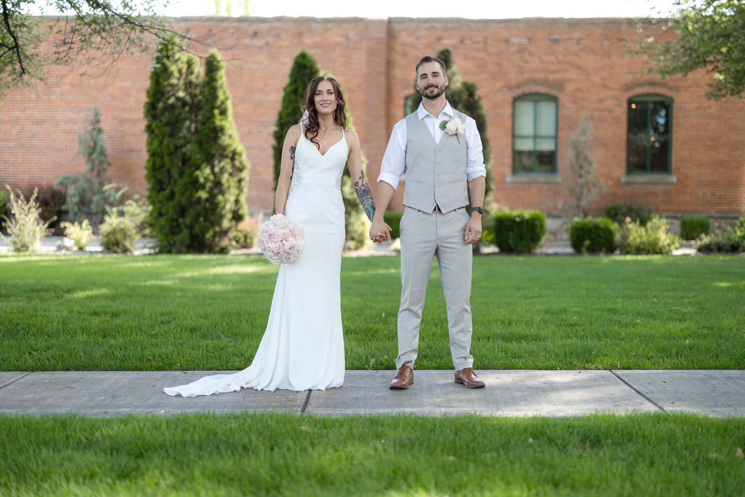 Wedding couple posing in front of a rustic brick building with landscaped garden.