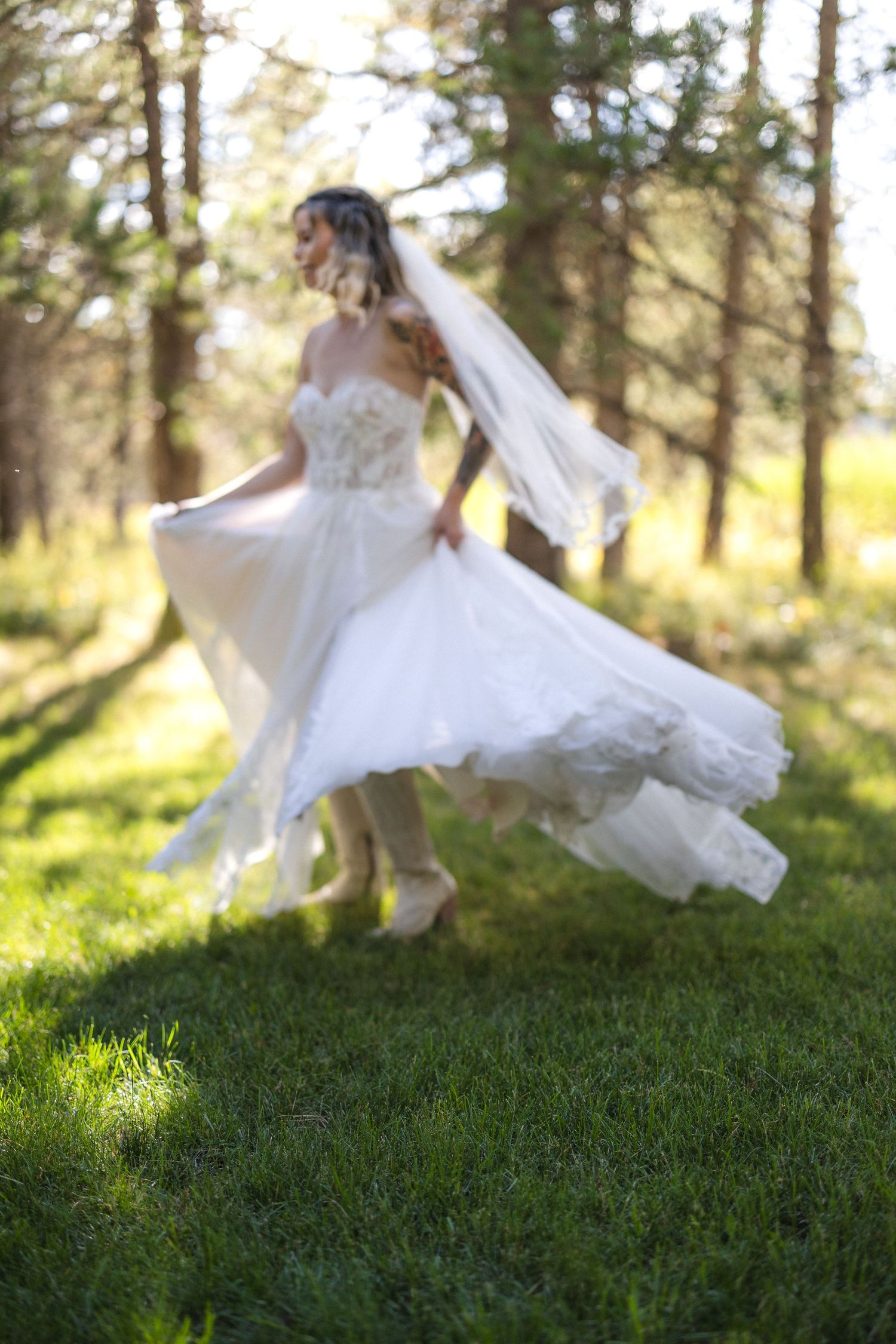 Ethereal photo of a bride twirling in her wedding dress in dappled forest light.