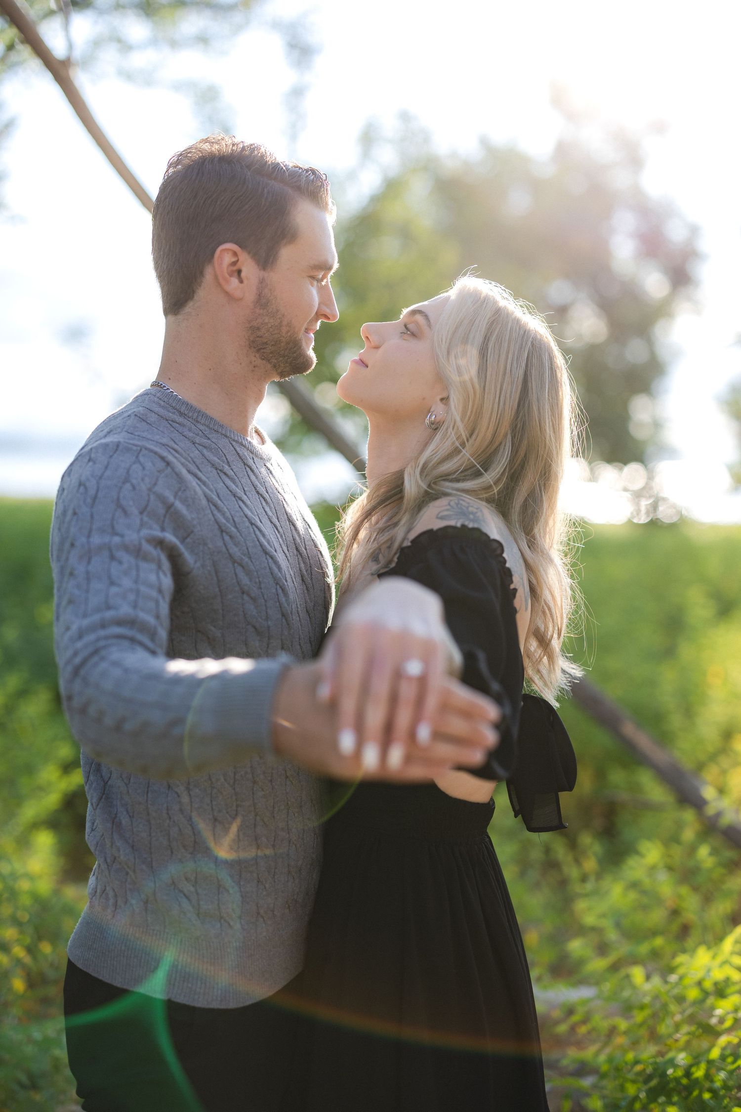 Couple in romantic embrace against sunlit nature backdrop with soft lighting effects.