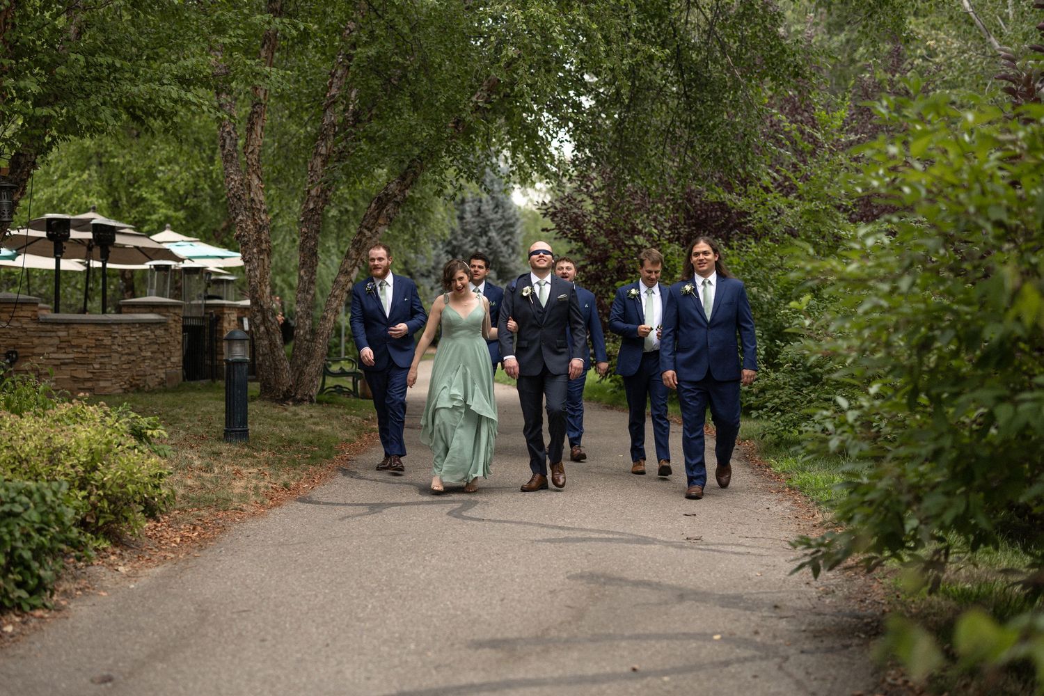 Wedding party members walk together down a tree-lined pathway.