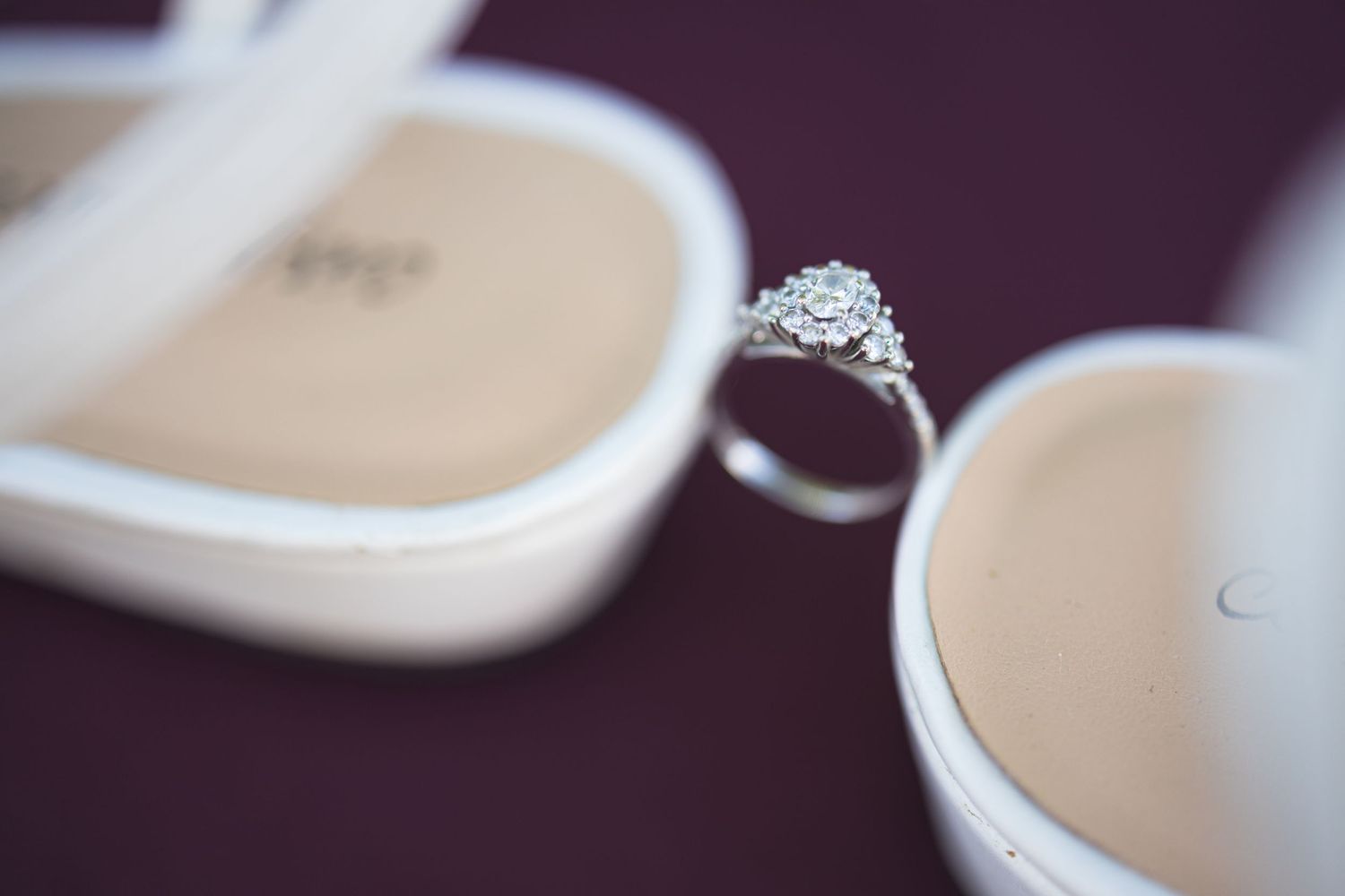 Diamond engagement ring balanced between white wedding shoes with blurred background.