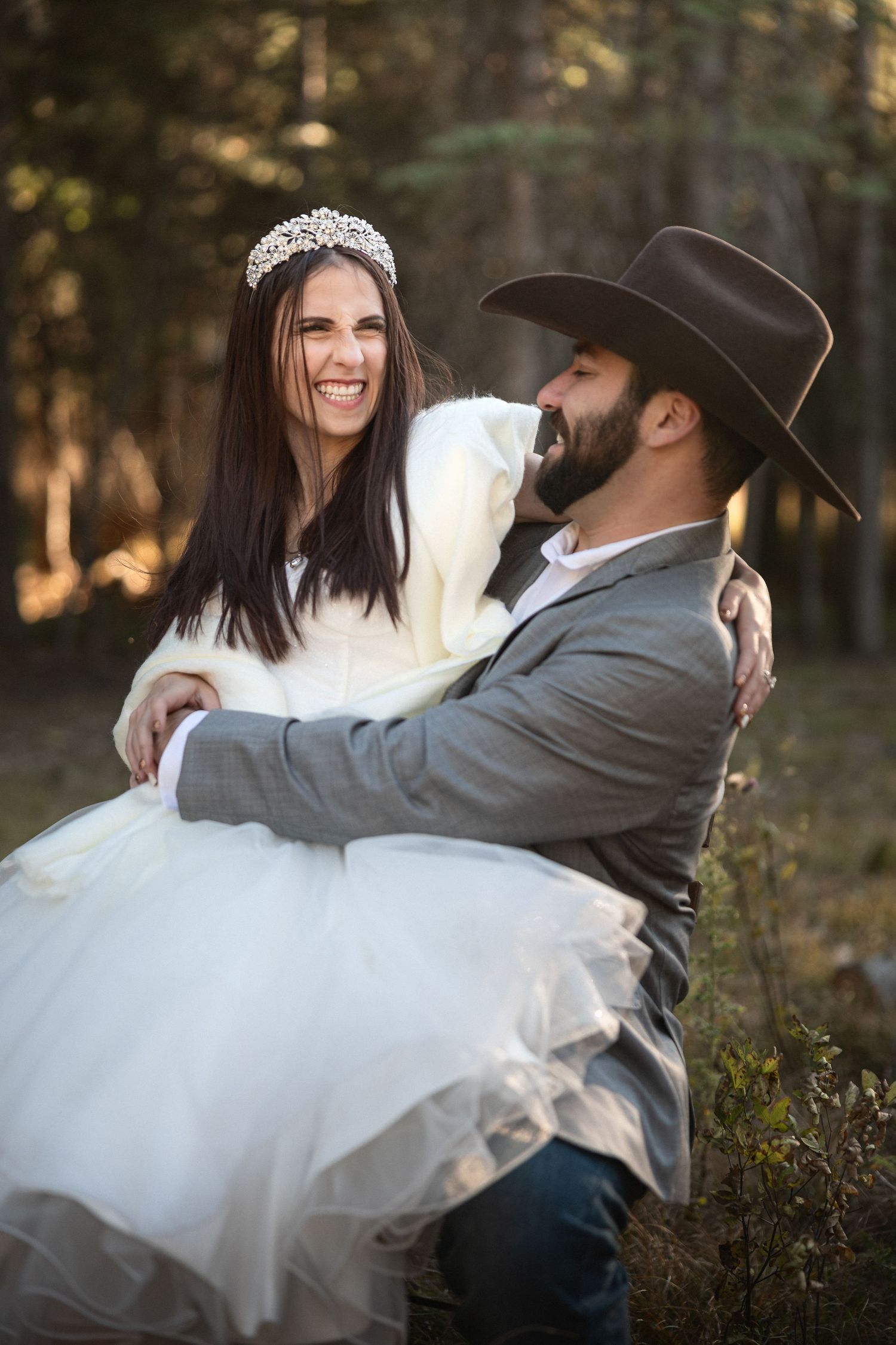 Joyful wedding portrait with bride in tiara and groom in cowboy hat embracing.