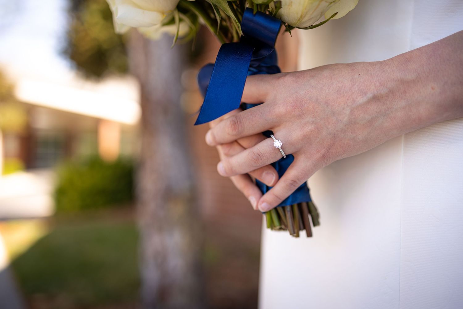 Close-up of hands holding wedding bouquet wrapped in royal blue ribbon.