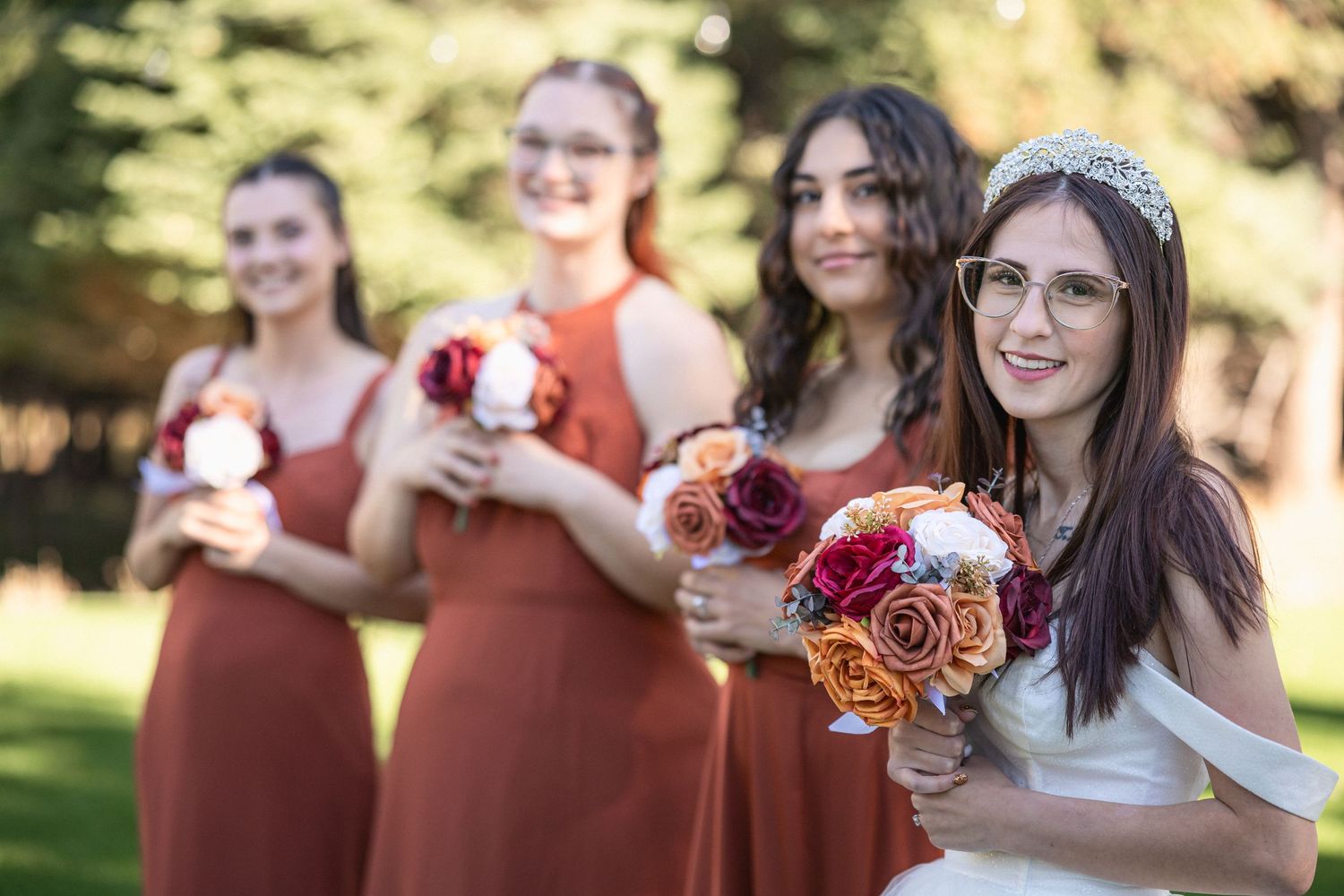 Wedding party poses with bouquets against evergreen trees in outdoor setting.