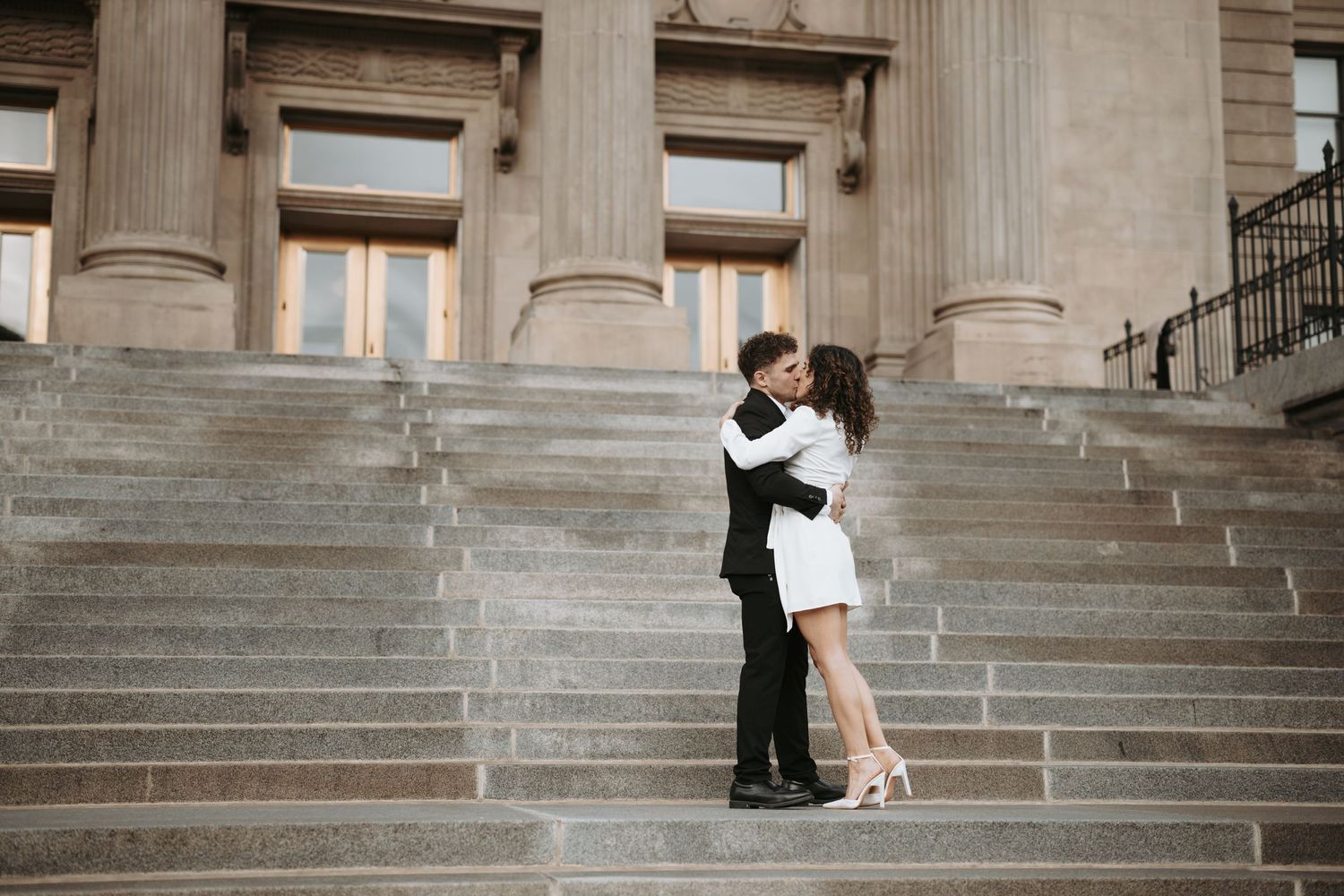 A couple in black and white formal wear embraces on grand stone steps.
