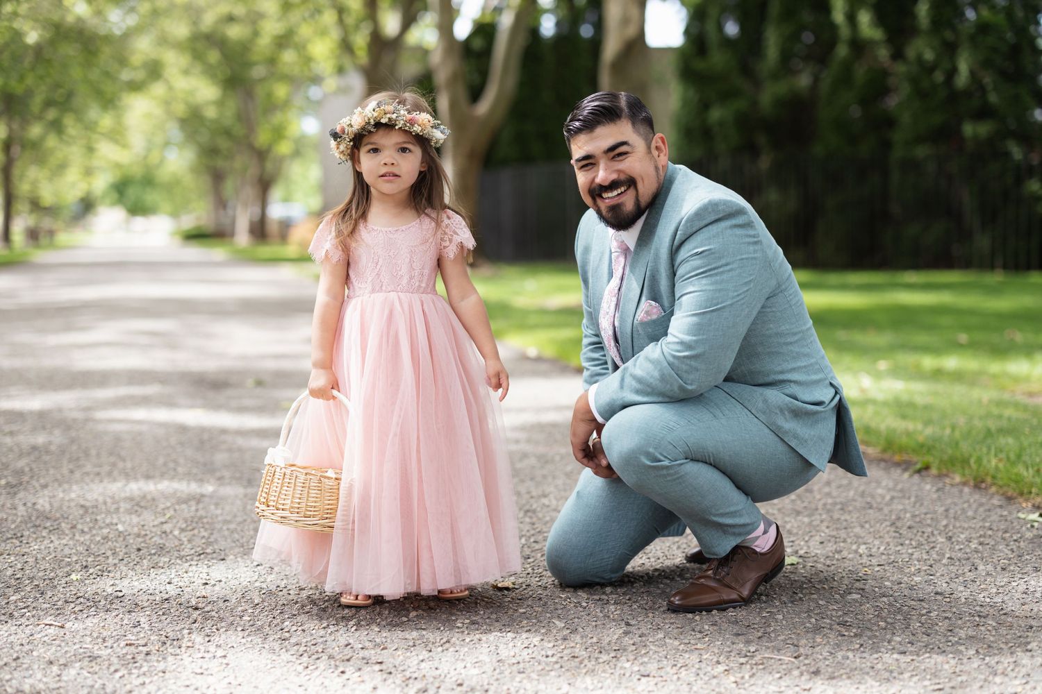 Young girl in pink dress and man in blue suit share sweet moment during outdoor wedding photoshoot.