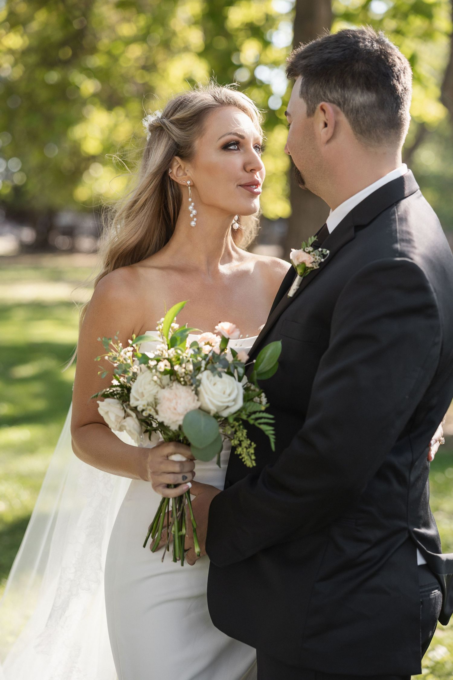 Wedding couple sharing intimate moment with white rose bouquet in garden setting.