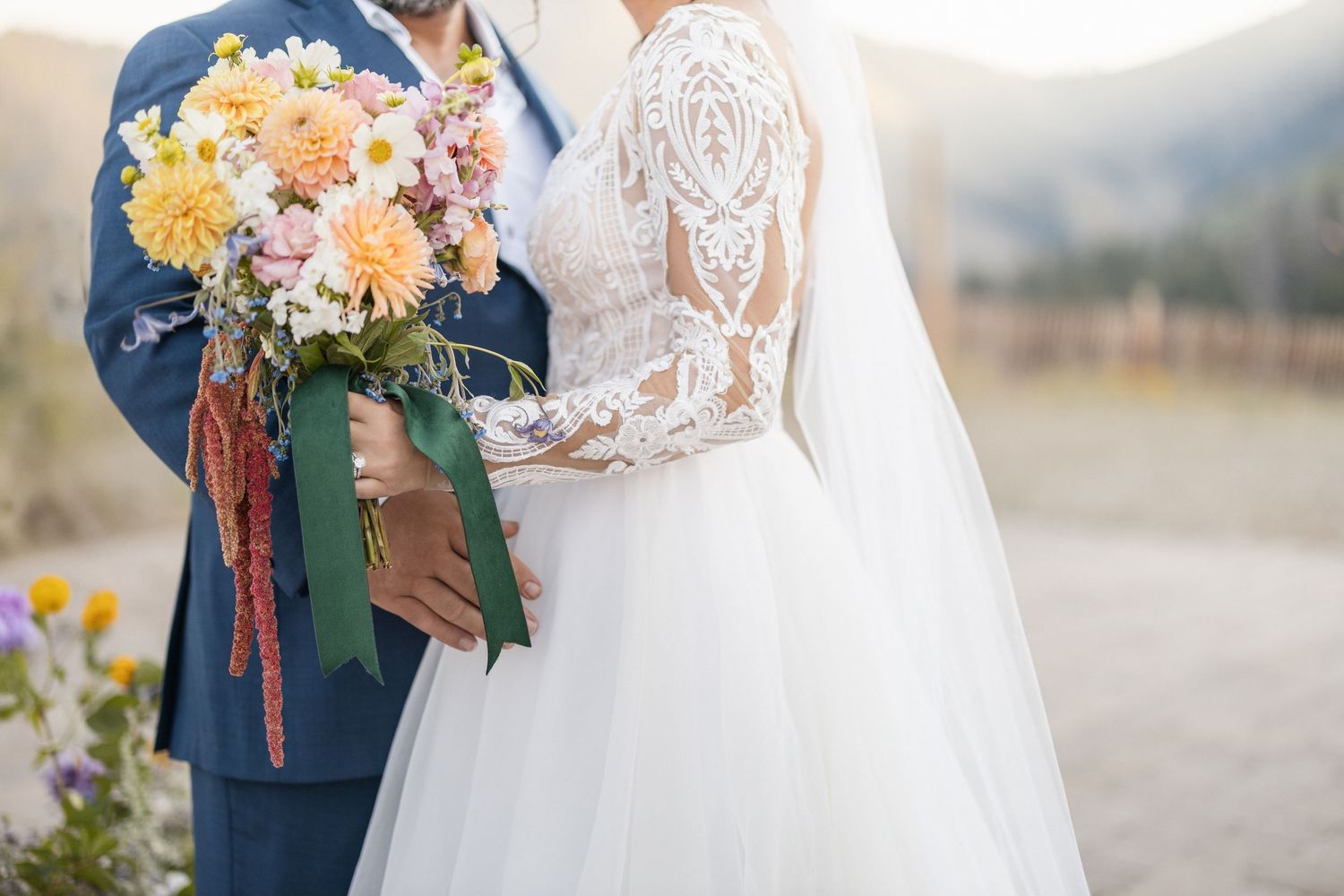 A white lace wedding dress and navy suit are captured in an intimate outdoor portrait.