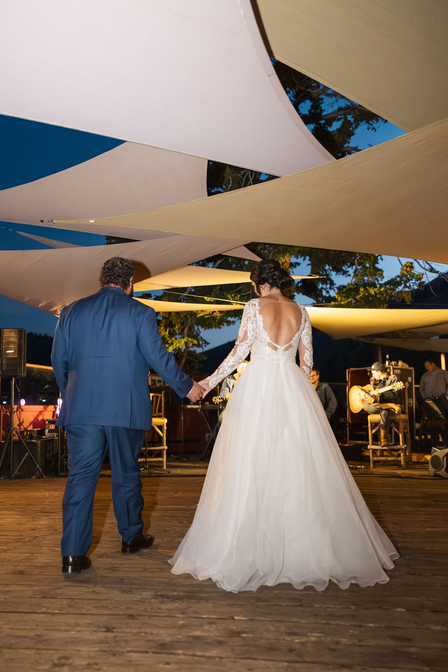 Wedding couple standing under white sail canopies at outdoor evening reception.