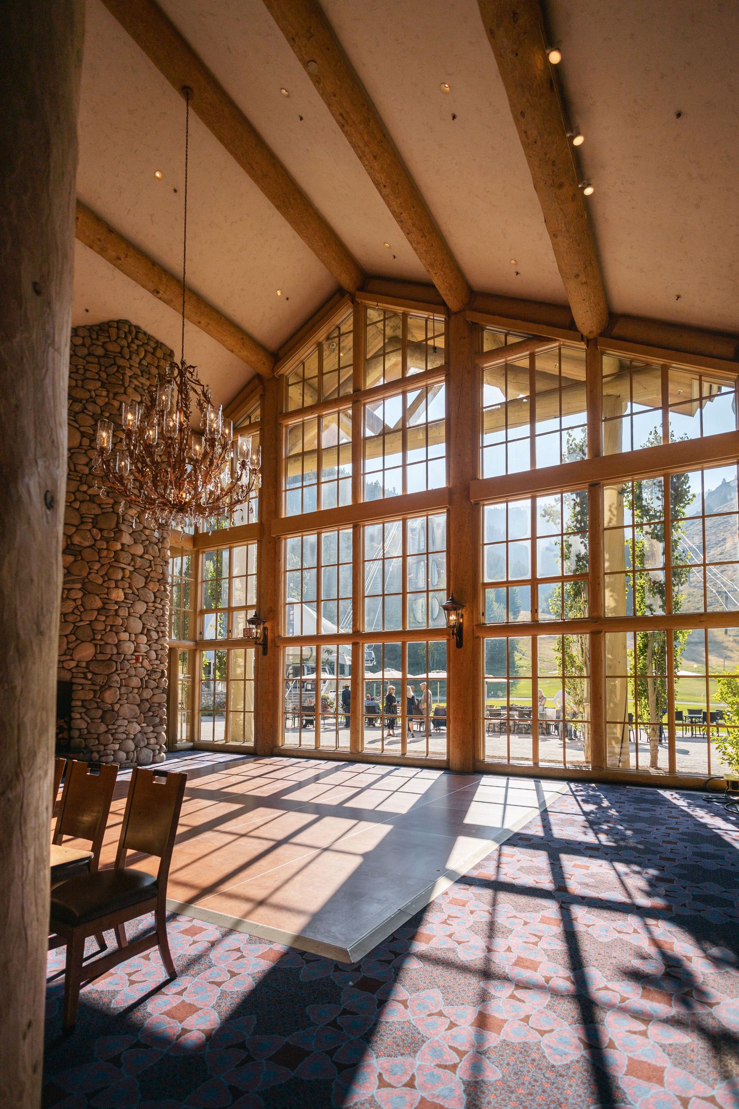 Modern mountain lodge interior with floor-to-ceiling windows and stone walls bathed in natural sunlight.
