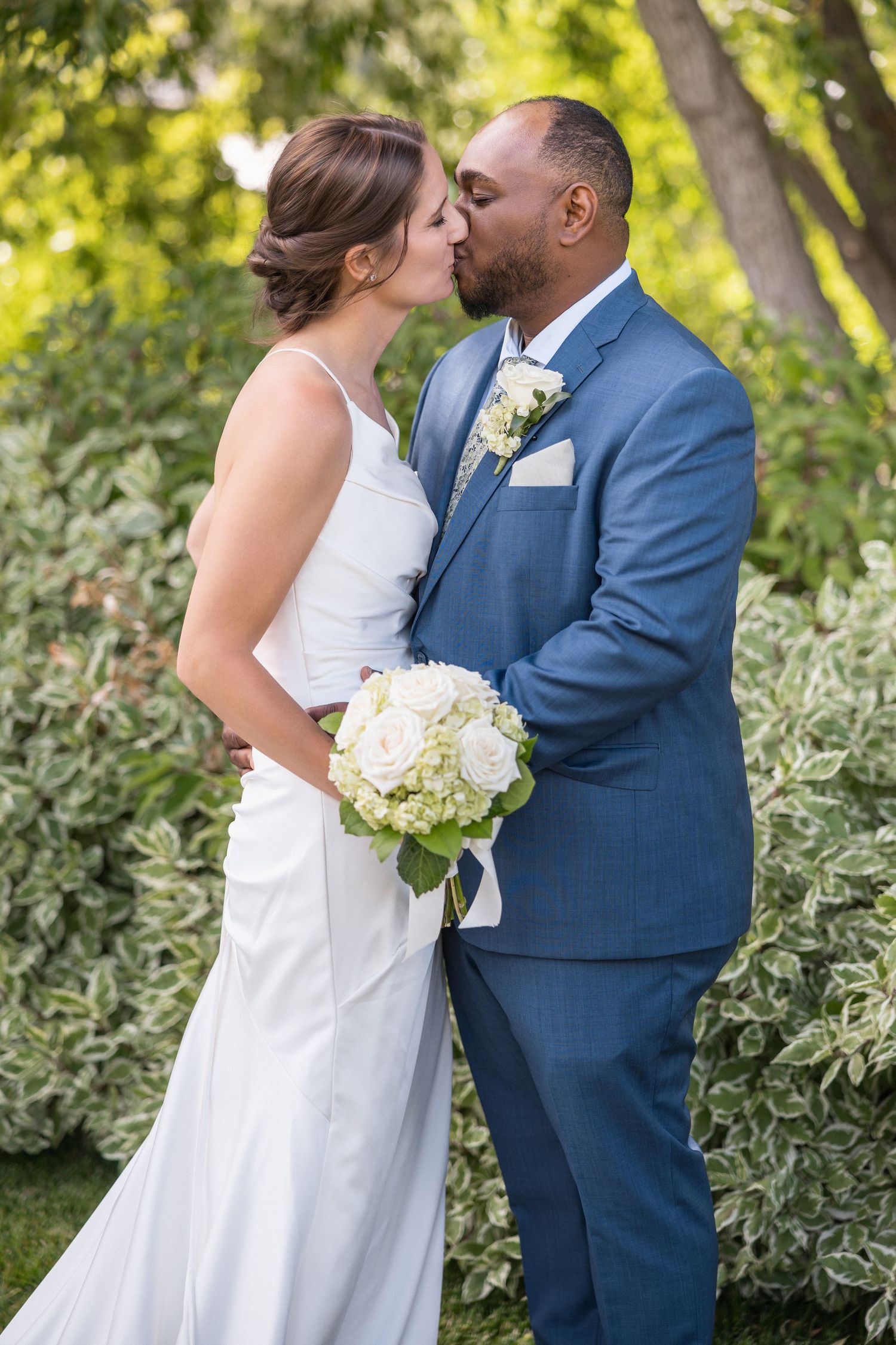 A tender wedding moment captured against a backdrop of lush garden foliage.