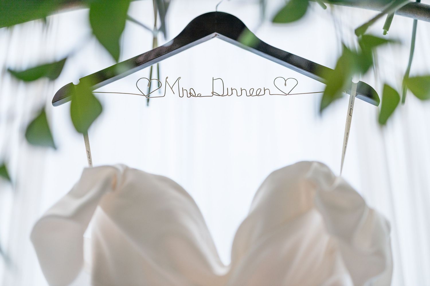 Elegant white floral arrangements with greenery decorate a wedding ceremony venue with draped fabric and chandeliers.