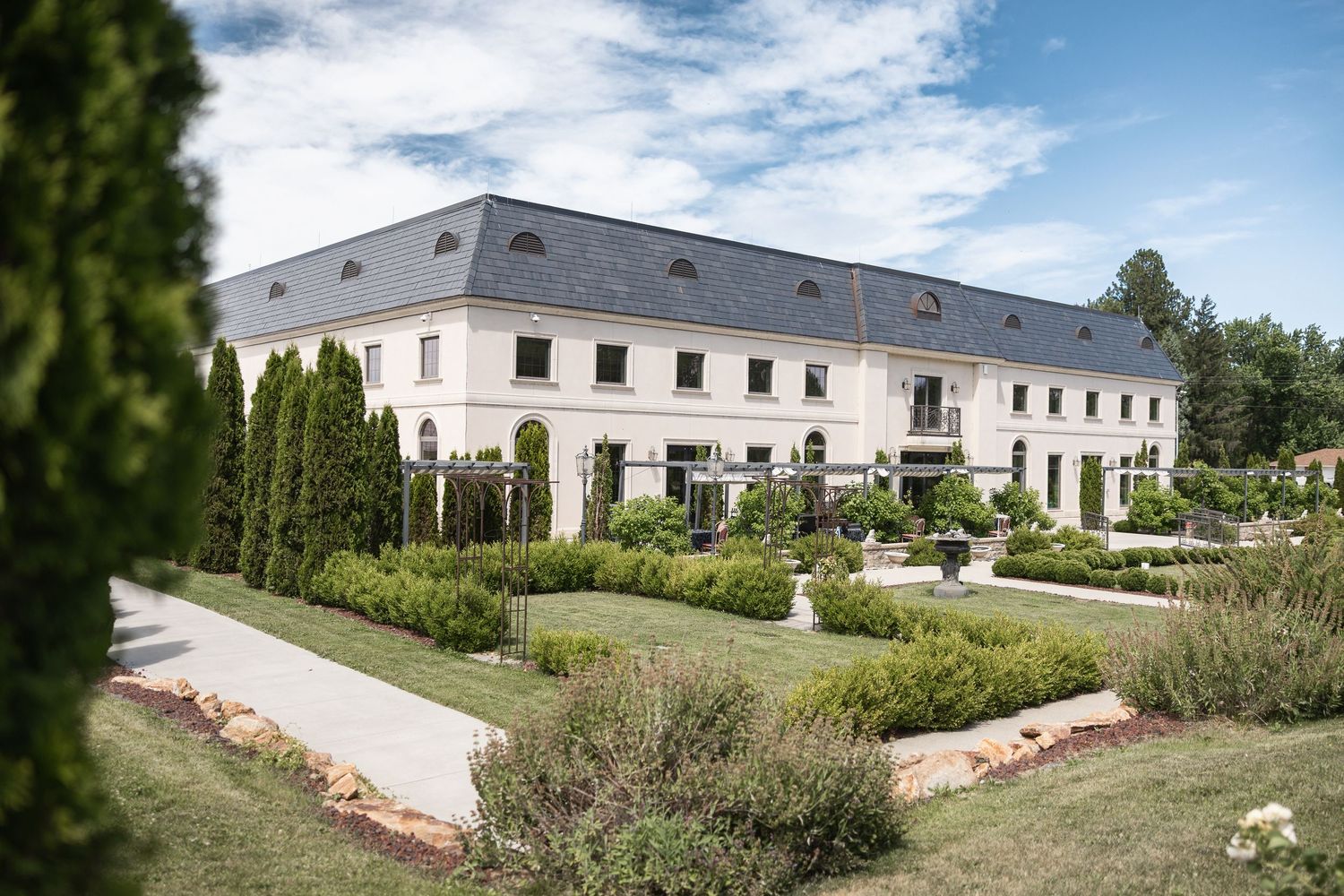 Panoramic view of a grand white estate building with landscaped gardens and cloudy sky.