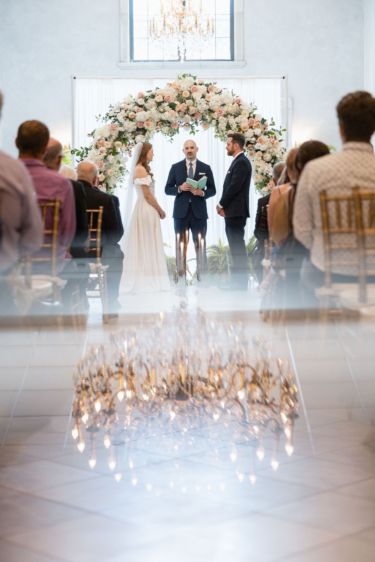 Dreamy wedding ceremony scene with chandelier creating bokeh effect over the proceedings.