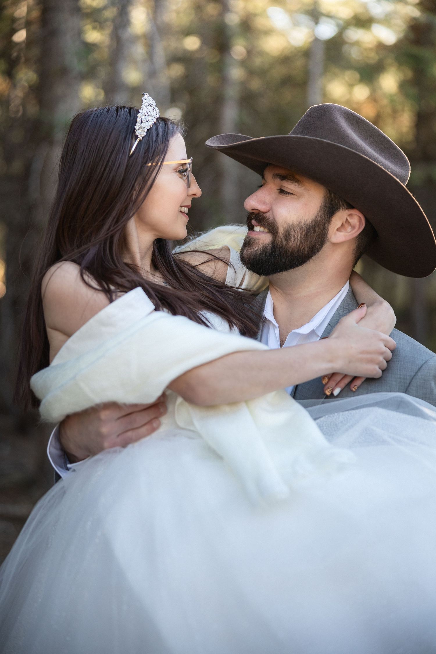 Romantic wedding couple embracing in a forest setting with cowboy hat and white dress.