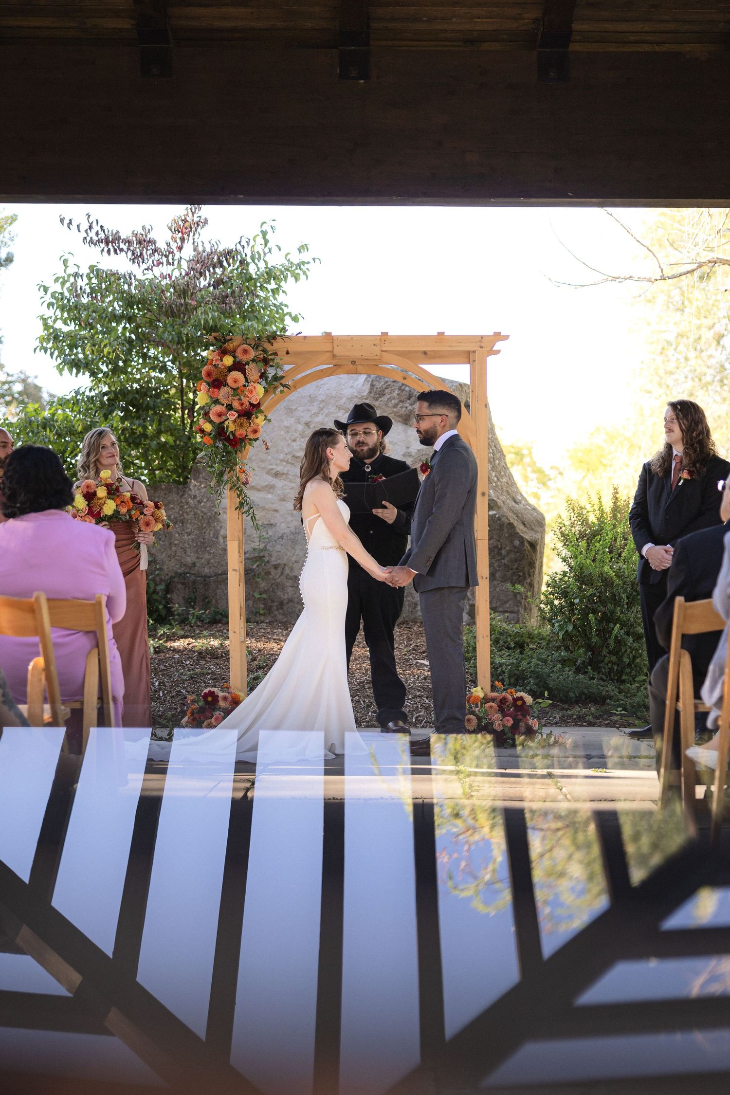 Wedding ceremony under wooden arch decorated with autumn flowers.