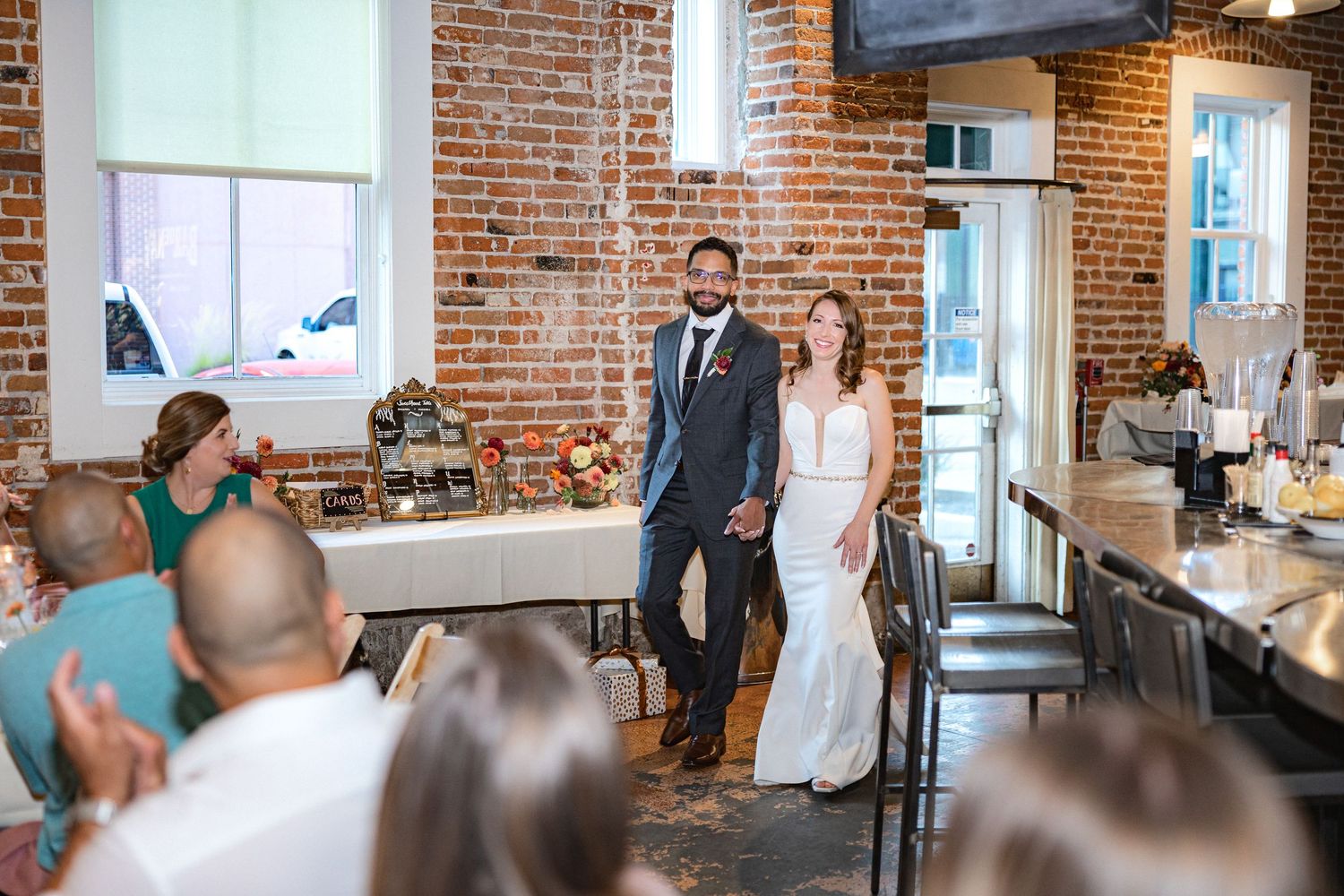 Wedding reception in brick-walled venue with industrial ceiling and natural lighting.