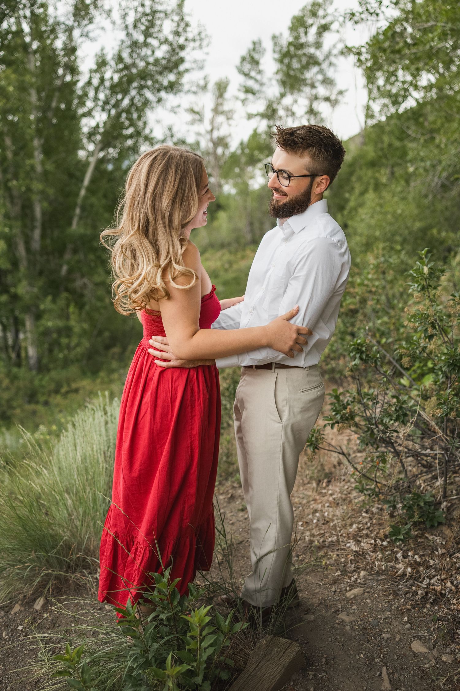 A couple shares a romantic moment on a nature trail surrounded by green trees and foliage.