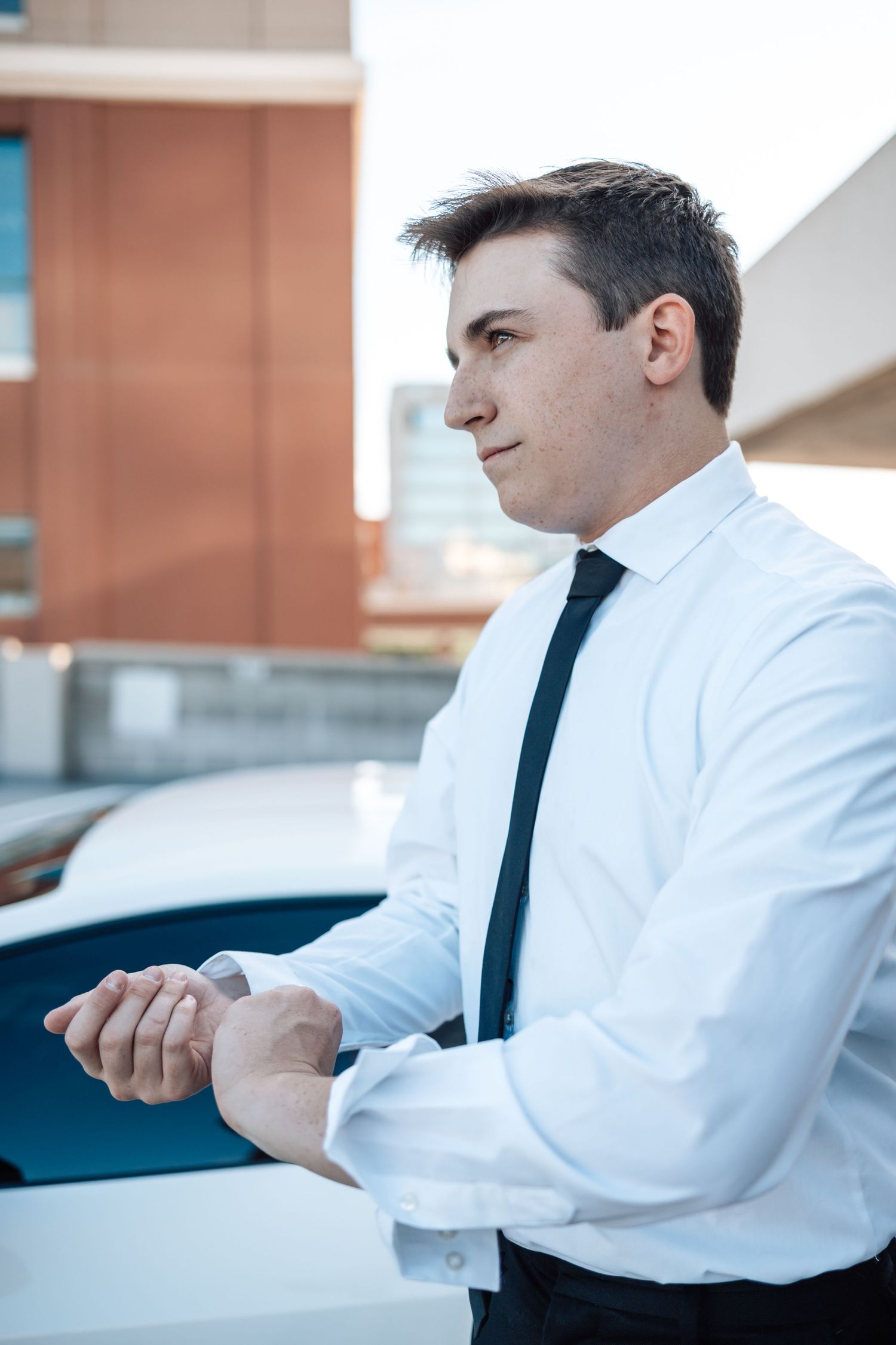 Professional in business attire adjusts sleeve cuff while standing in a parking structure.