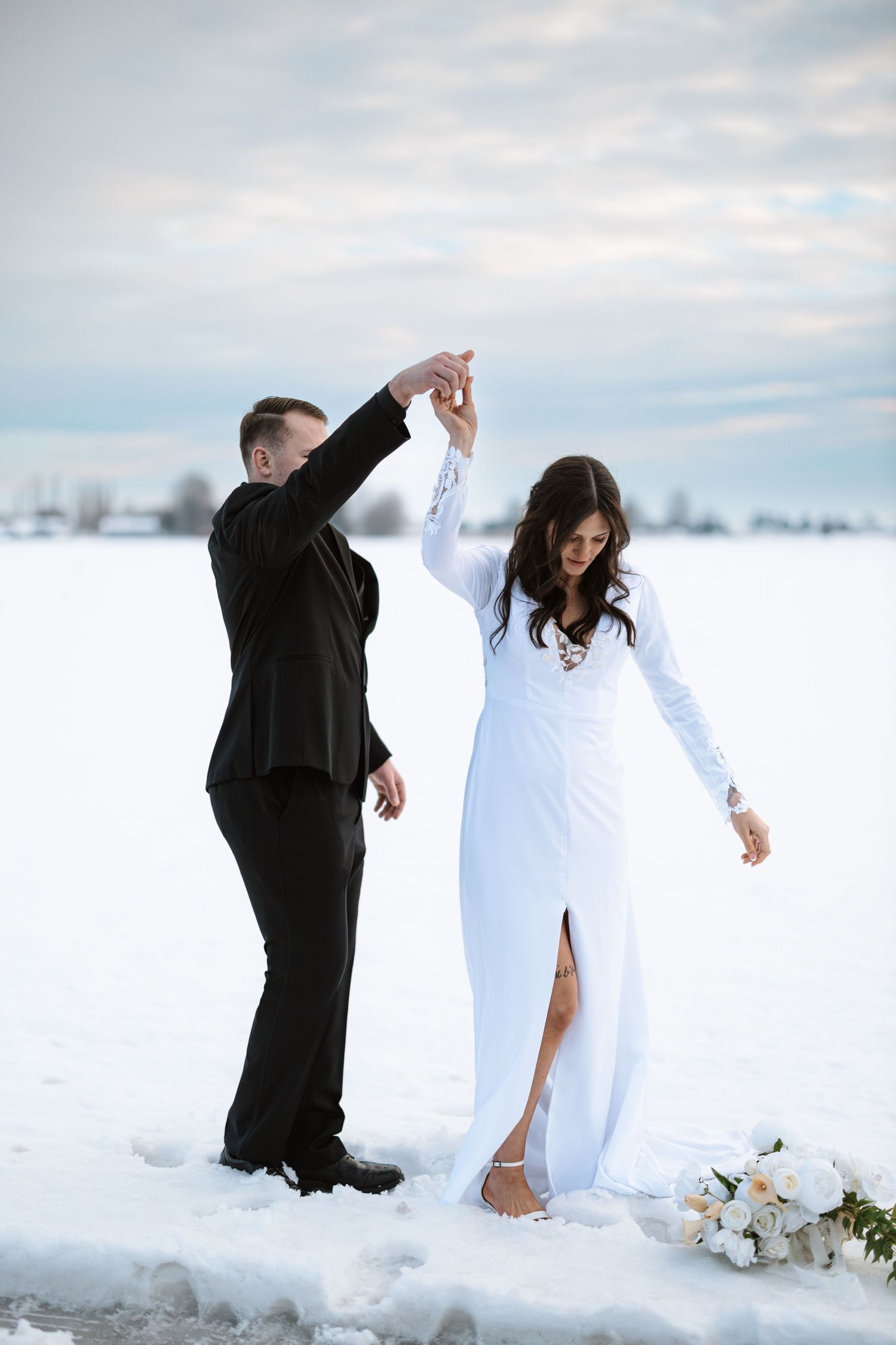 A couple dancing in formal attire against a snowy winter backdrop with a bouquet of flowers on the ground.