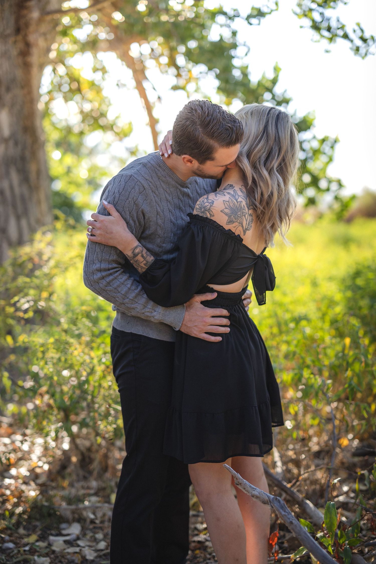 Romantic couple sharing intimate kiss outdoors in stylish casual attire.