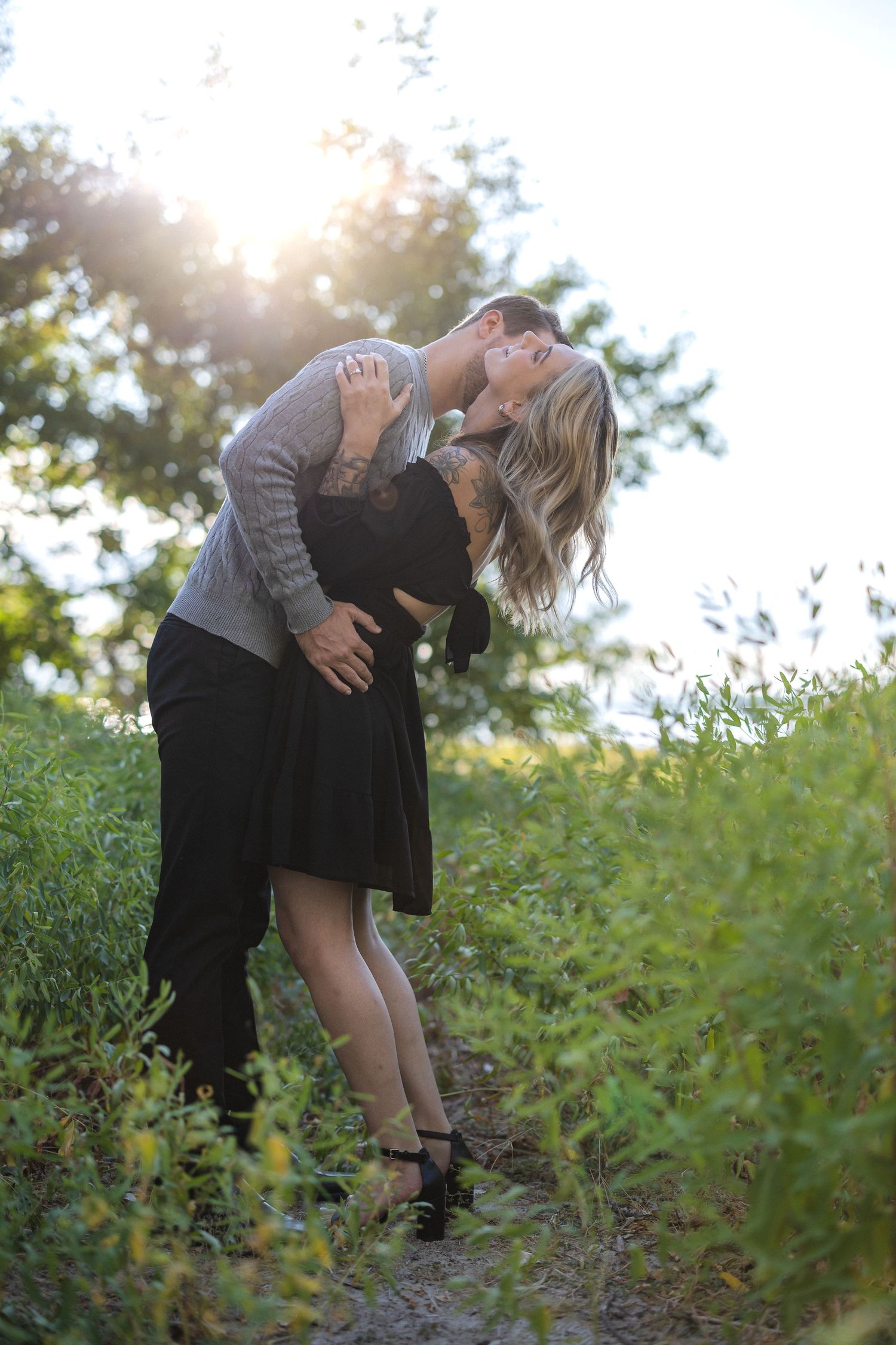 Romantic dip pose outdoors with couple in casual attire against natural backdrop.