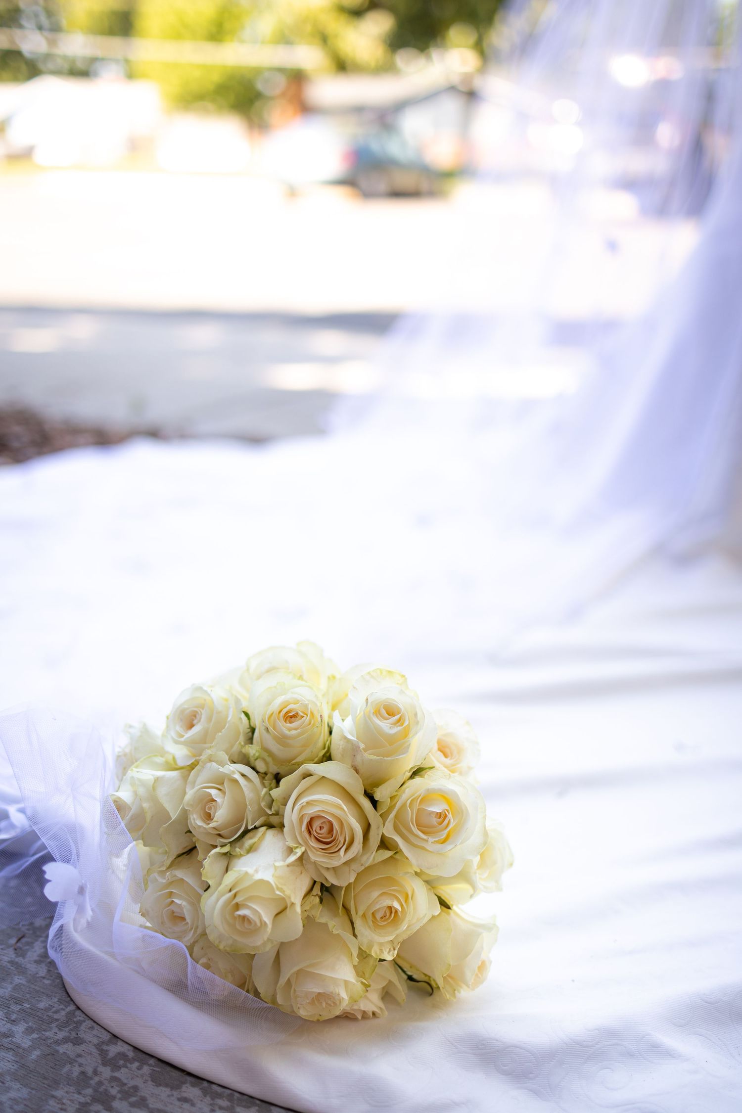 Close-up of an elegant white rose bridal bouquet resting on white fabric with soft bokeh background.